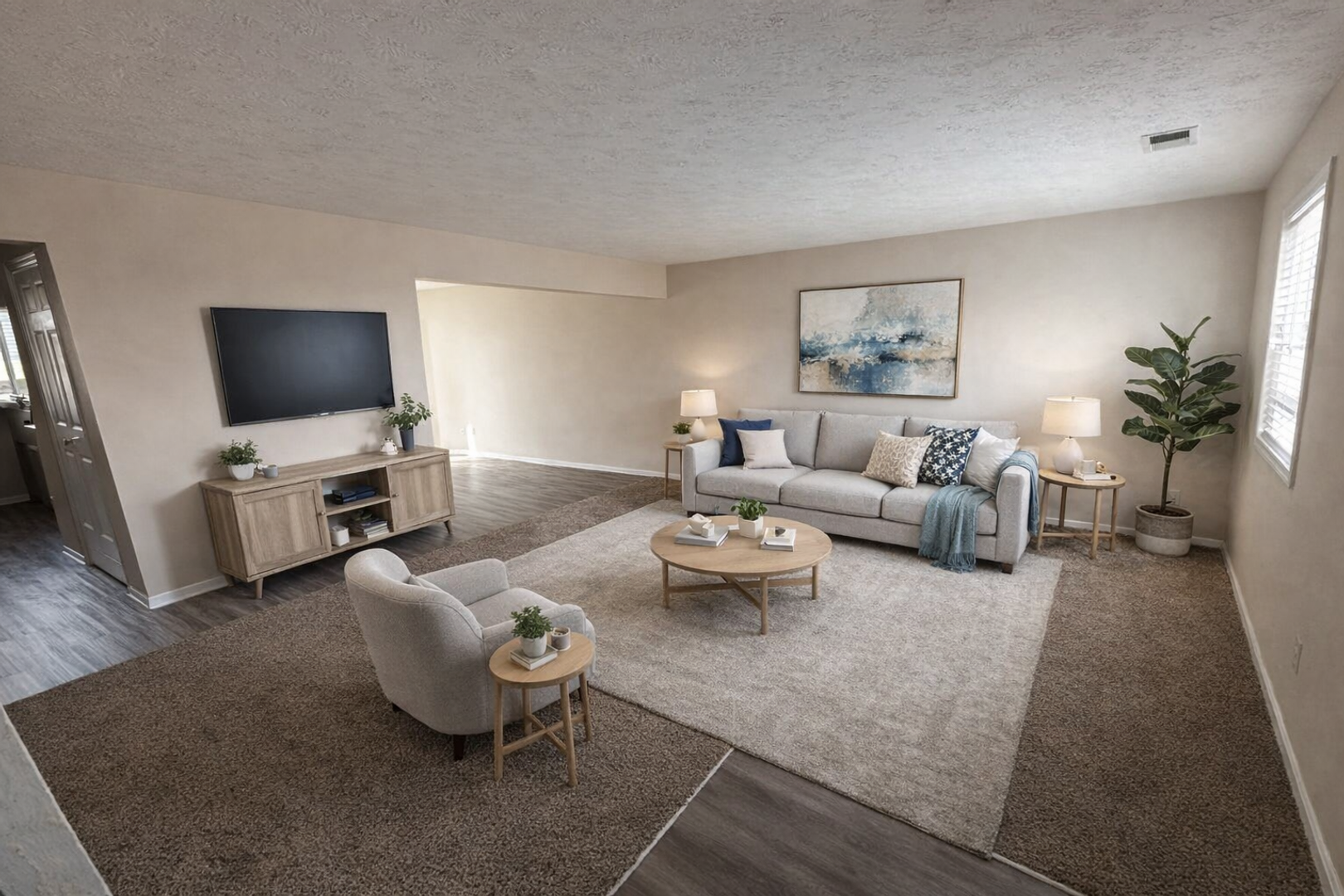 A modern living room with light walls, gray sofa, armchair, area rug, wooden media console, and a tall potted plant.