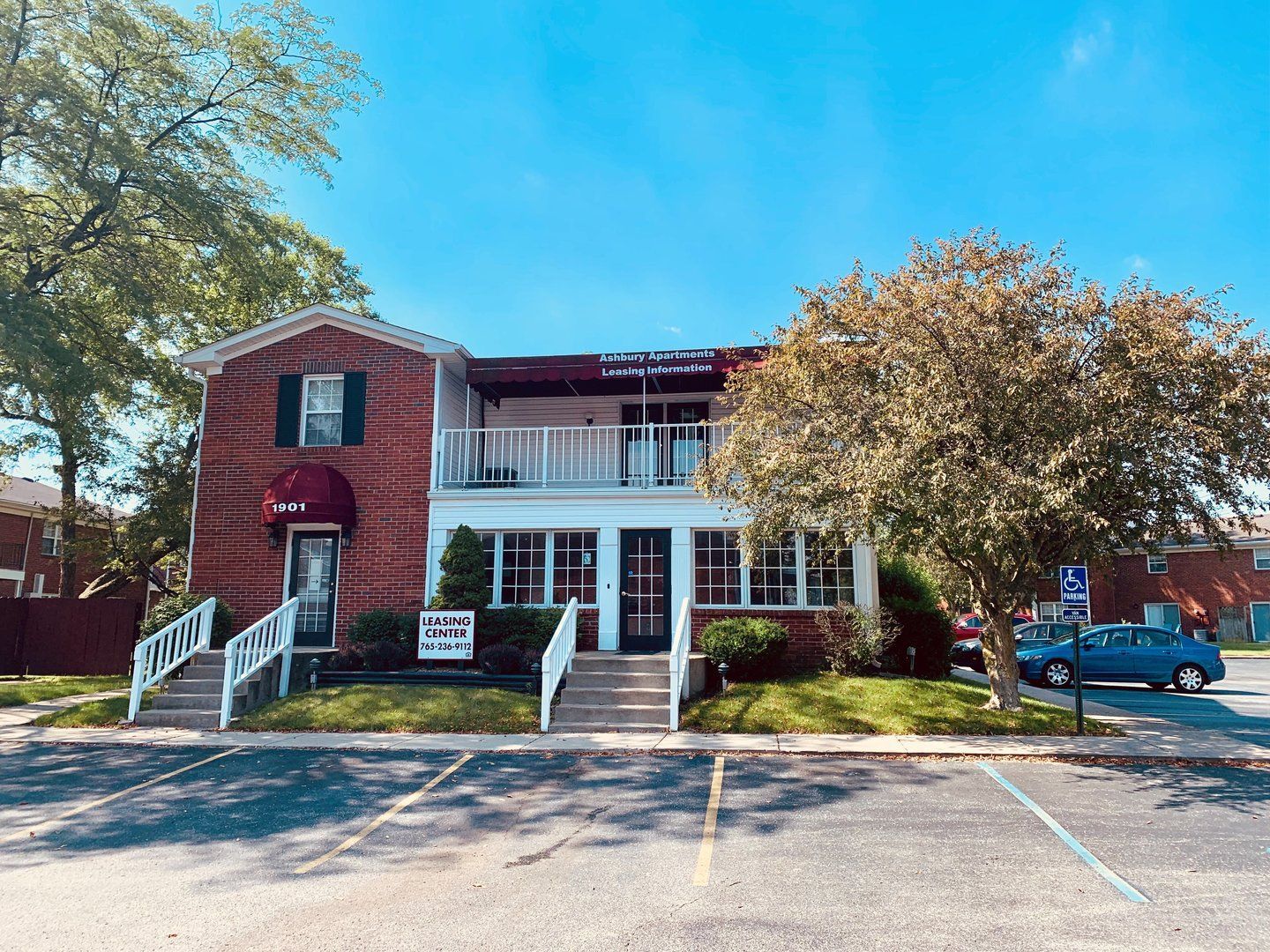 A two-story brick and white building under a clear blue sky, featuring a balcony, two staircases, and a parking lot.