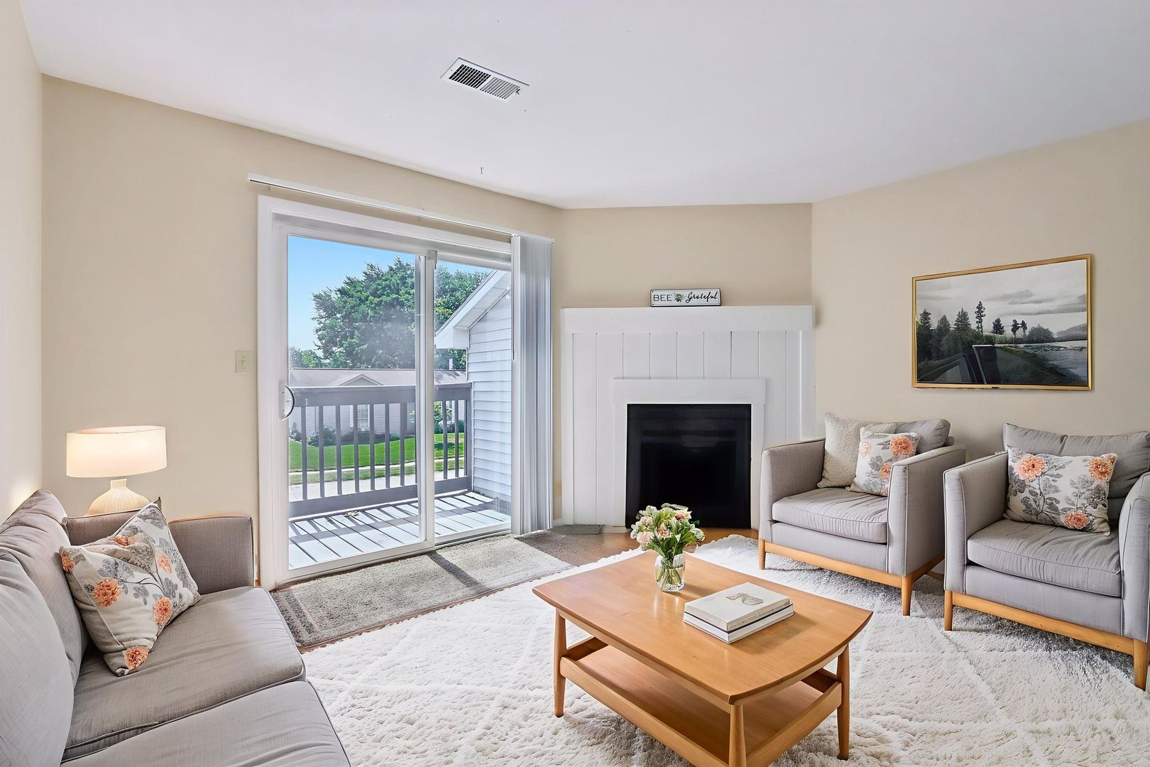 Living room with two armchairs, a couch, a coffee table with flowers, and a sliding glass door leading to a balcony.