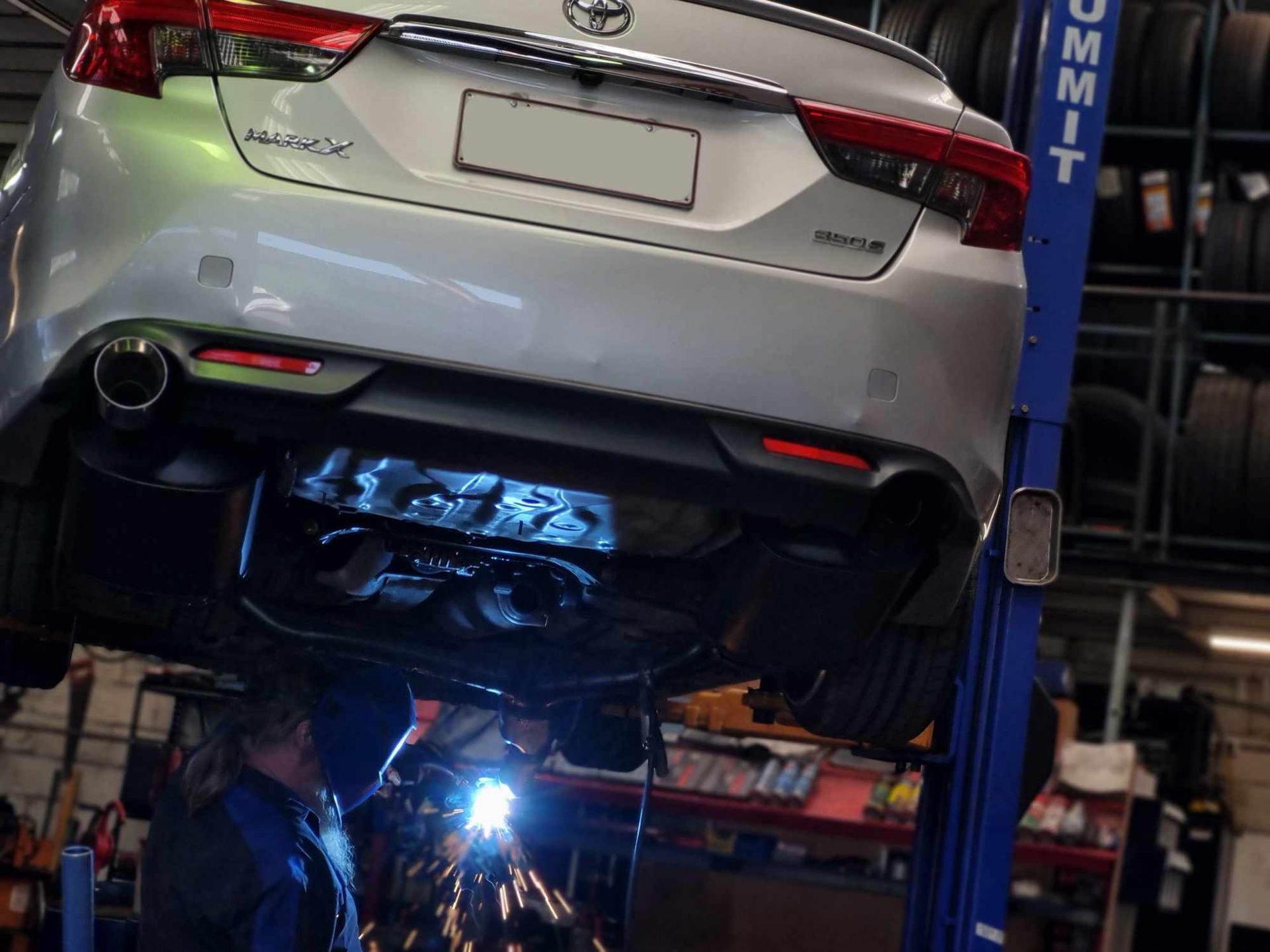 A Man is Working on the Underside of a Car on a Lift — BJM Mechanical Mufflers & Tyres In Oxenford, QLD