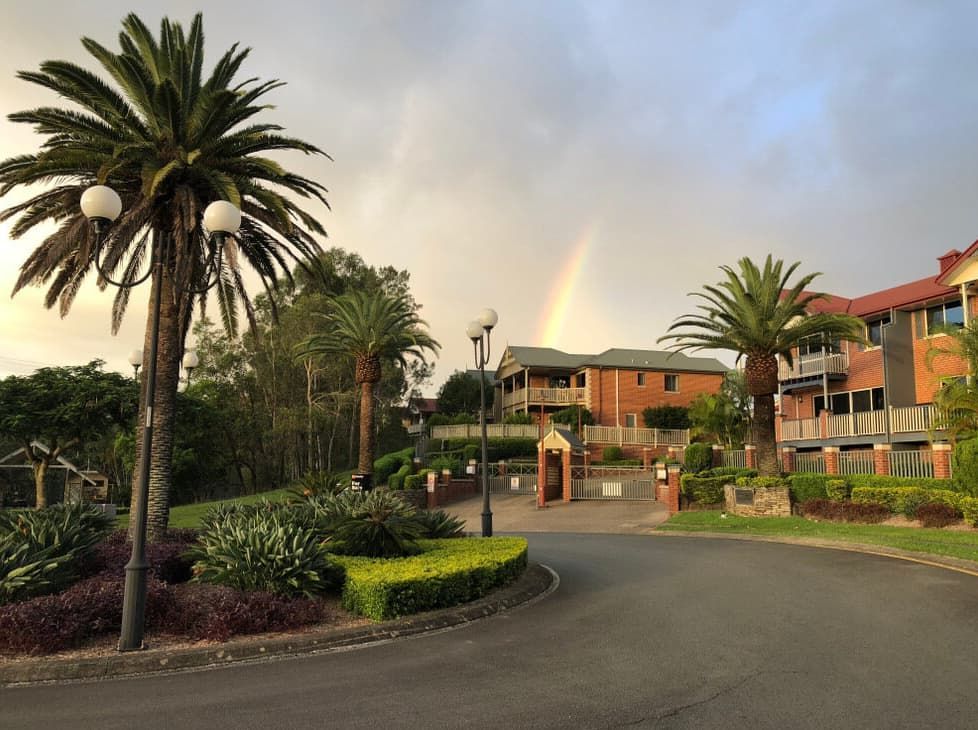 A Rainbow is Visible Over a Residential Area With Palm Trees — BJM Mechanical Mufflers & Tyres In Oxenford, QLD