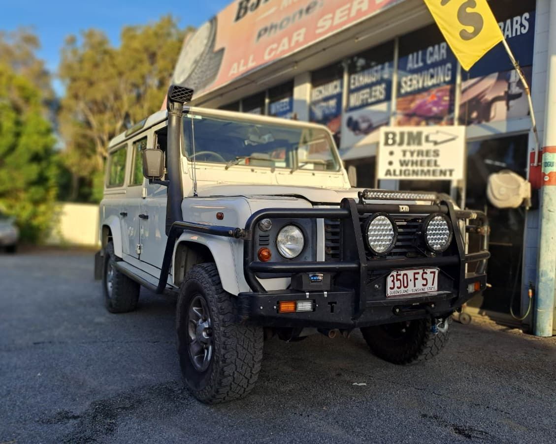 A White Jeep is Parked in Front of a Building That Says Bjm — BJM Mechanical Mufflers & Tyres In Oxenford, QLD