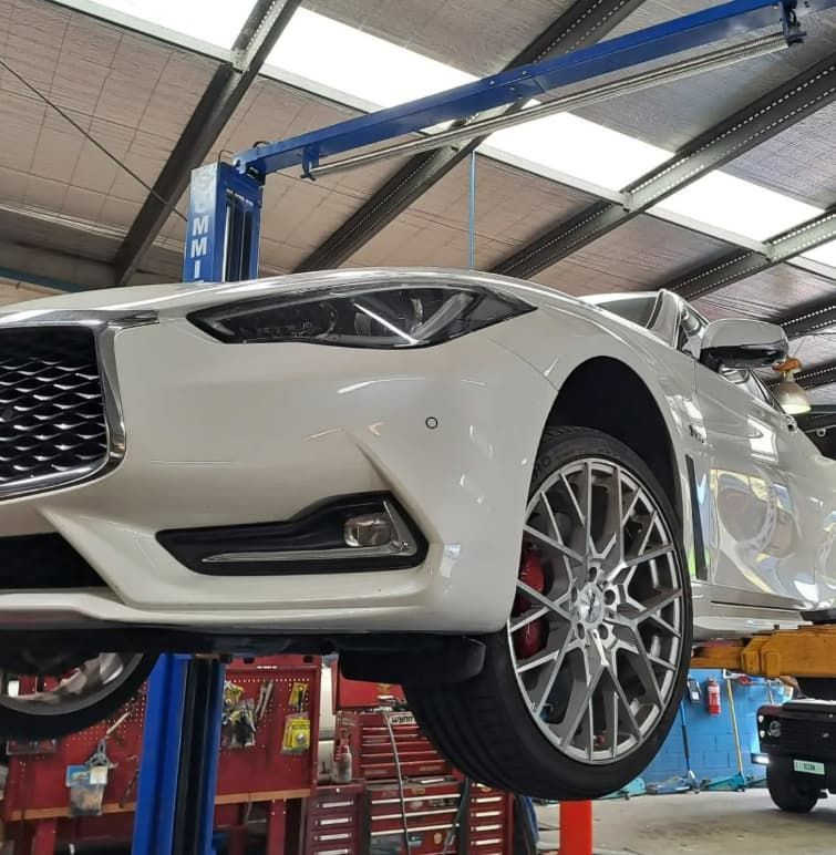 A White Sports Car is on a Lift in a Garage — BJM Mechanical Mufflers & Tyres In Oxenford, QLD