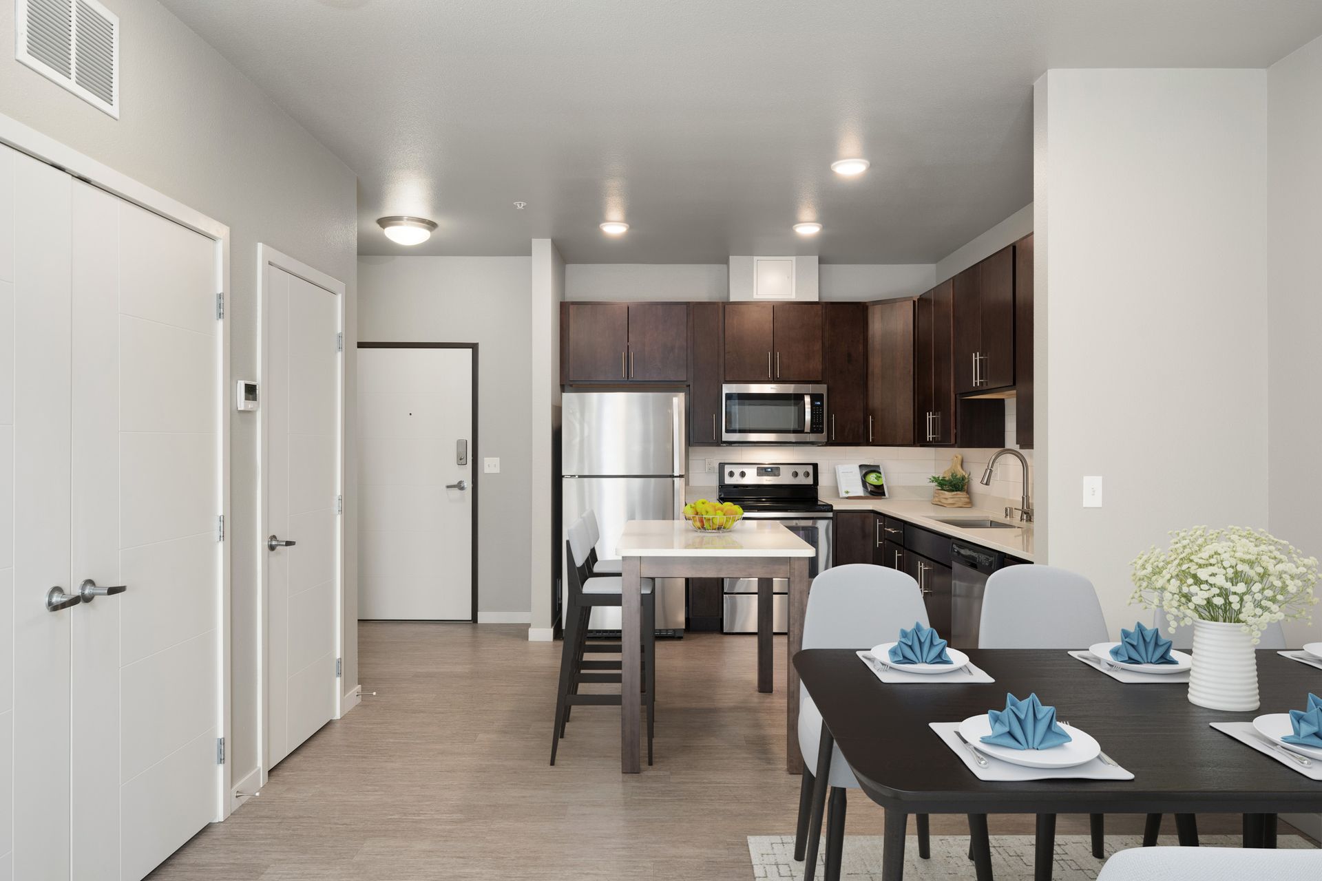 Modern apartment kitchen and dining area with dark cabinets, stainless steel appliances, and a table set for dining.