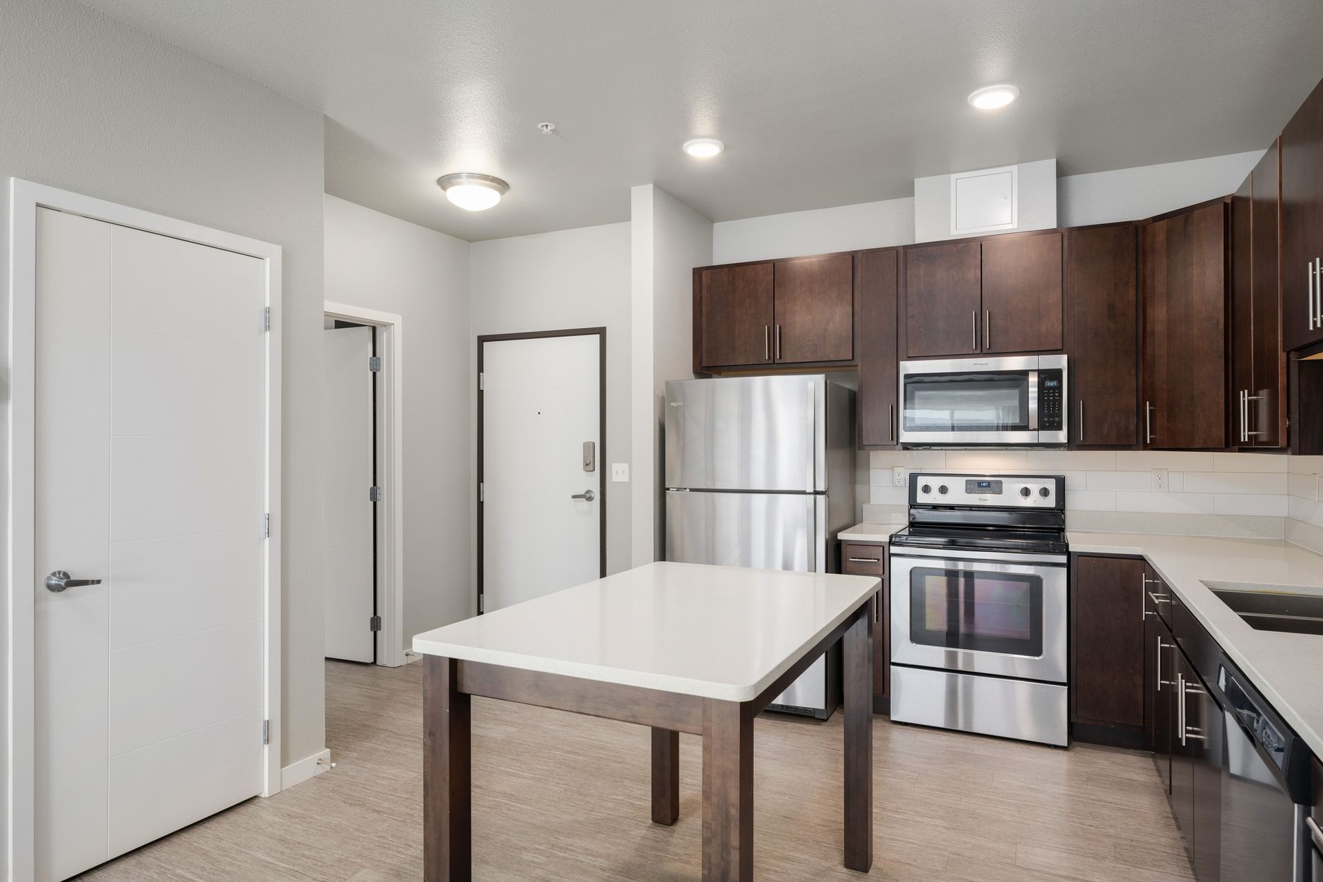 Modern kitchen with stainless steel appliances, dark wood cabinets, and white island.