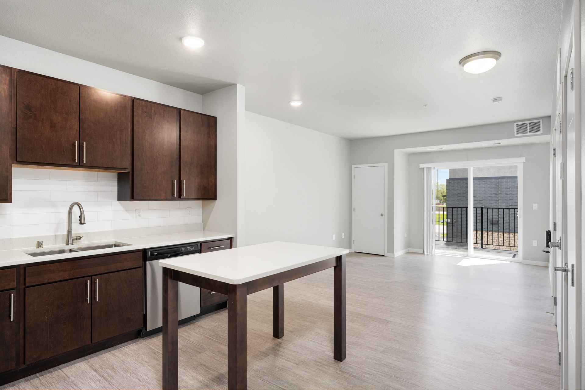 Modern kitchen with dark brown cabinets, white countertops, and an island. Sliding glass door to a balcony.