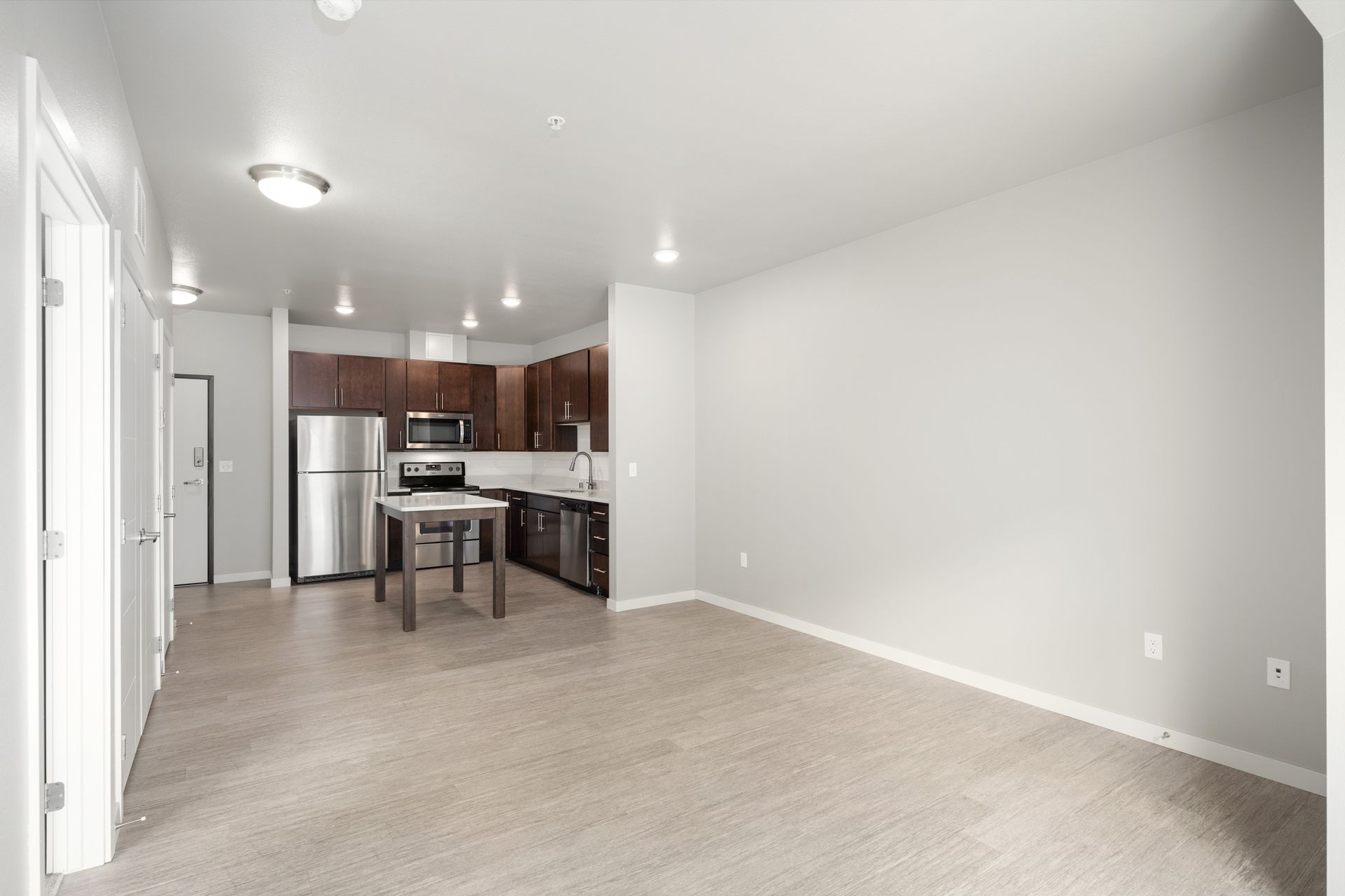 Empty apartment interior with kitchen, stainless steel appliances, and gray walls.