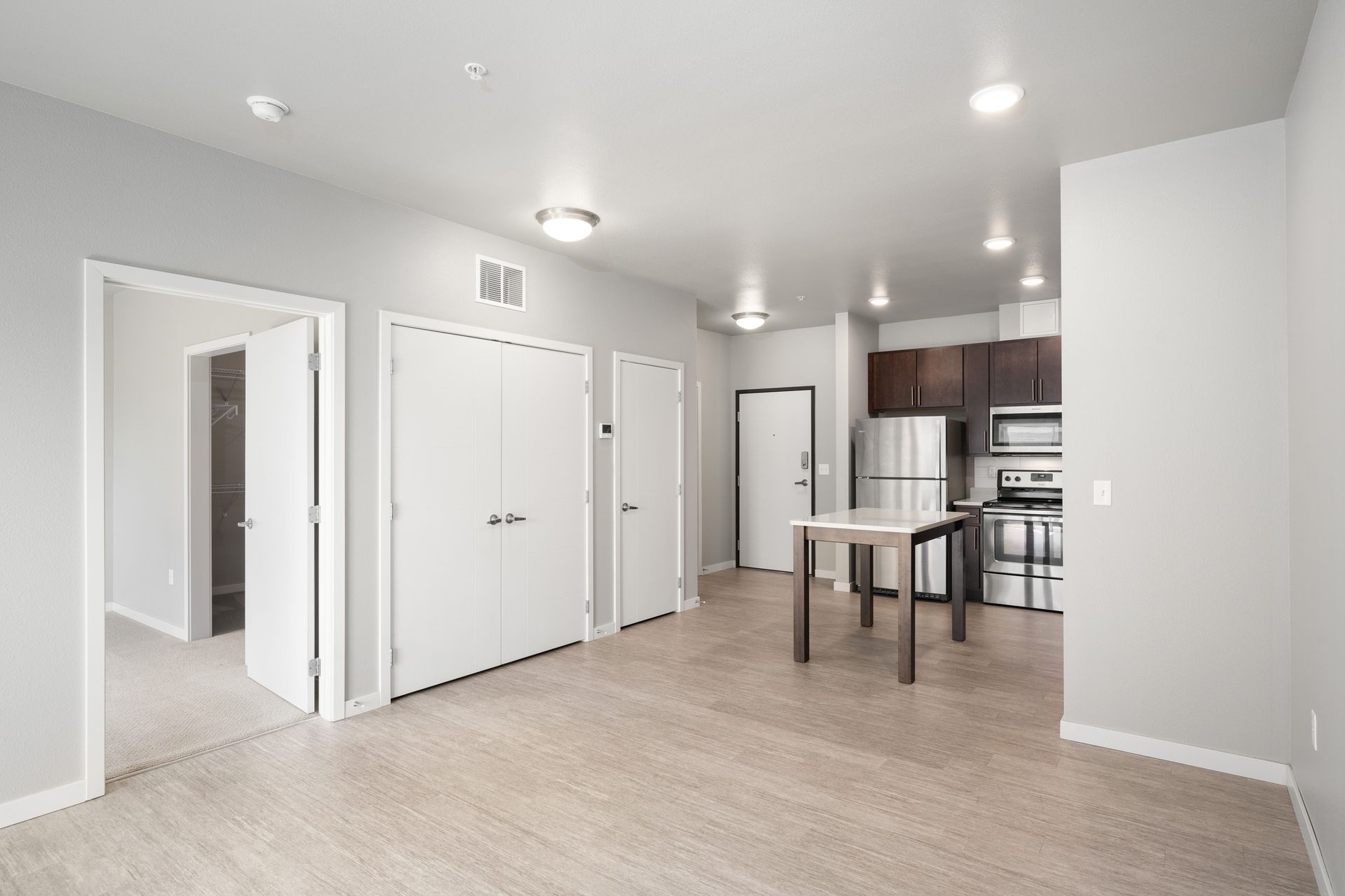 Empty apartment with open kitchen, stainless steel appliances, and white cabinets and doors.