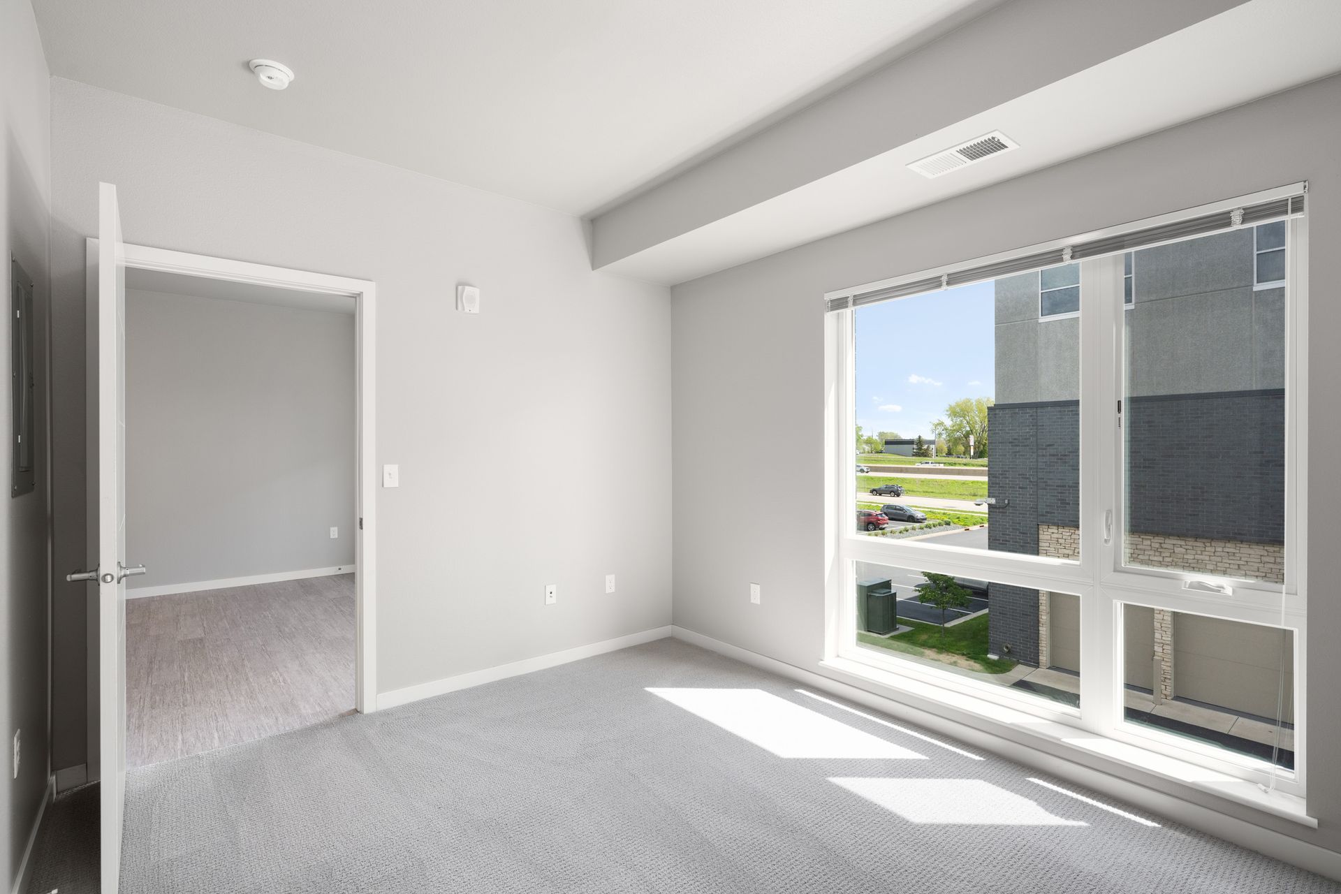 Empty bedroom with large window, open door, and light gray carpet.
