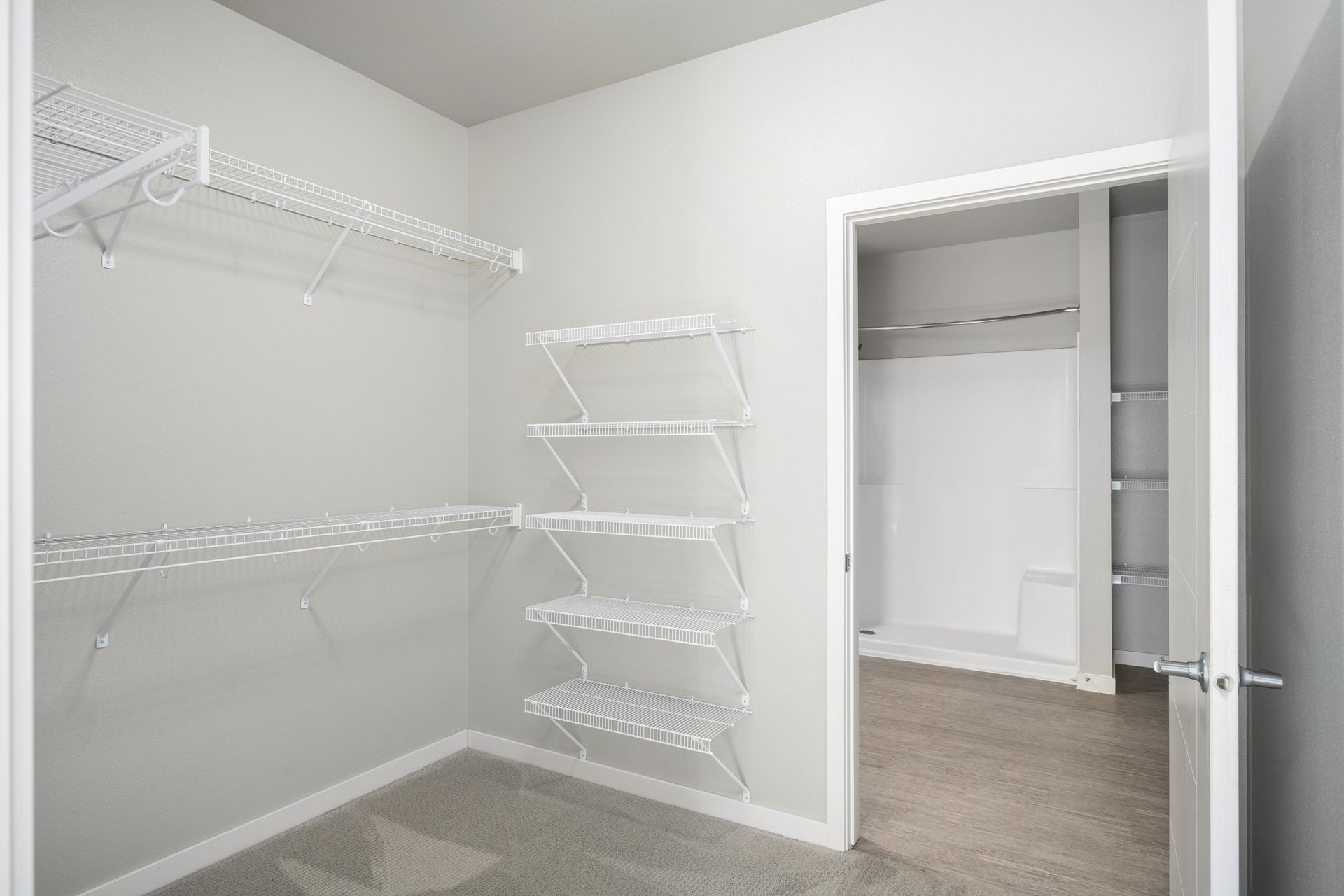 Empty walk-in closet with wire shelving on gray walls, carpeted floor, and doorway to another closet.