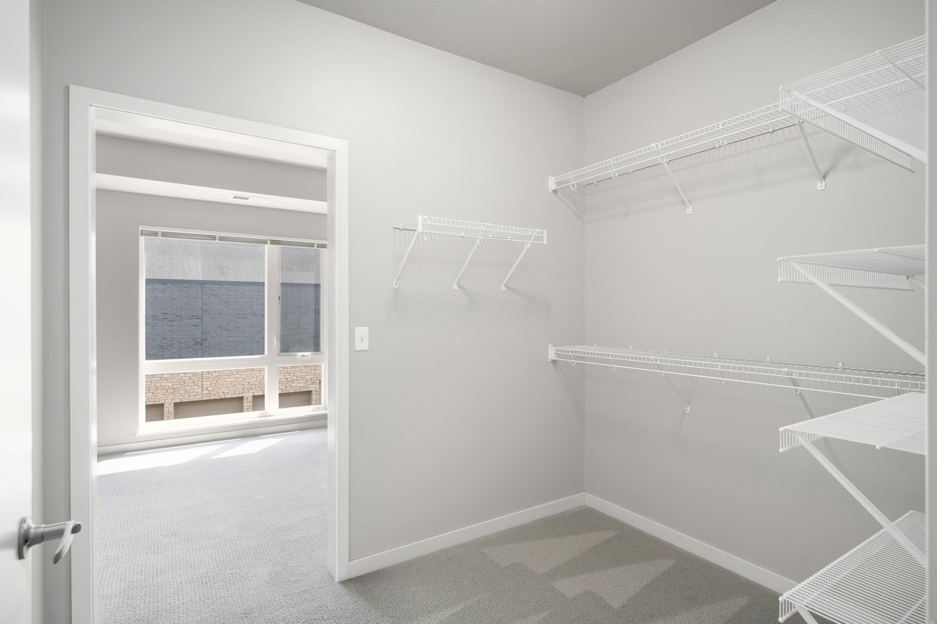 Empty walk-in closet with wire shelving and a doorway leading to a room with a window.