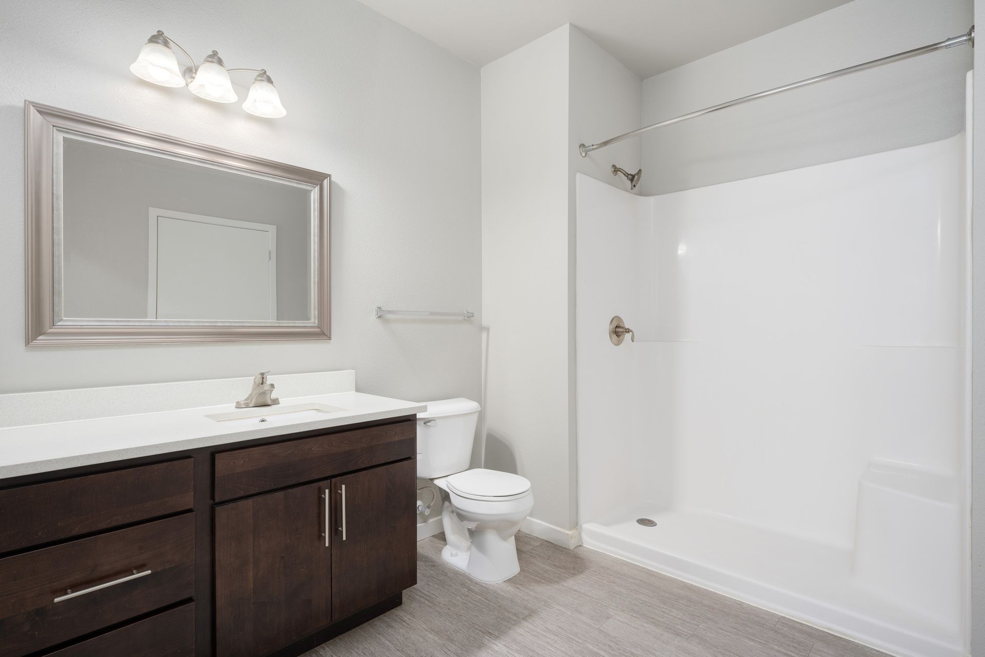 Bathroom with dark brown vanity, white countertop, large mirror, and white shower.