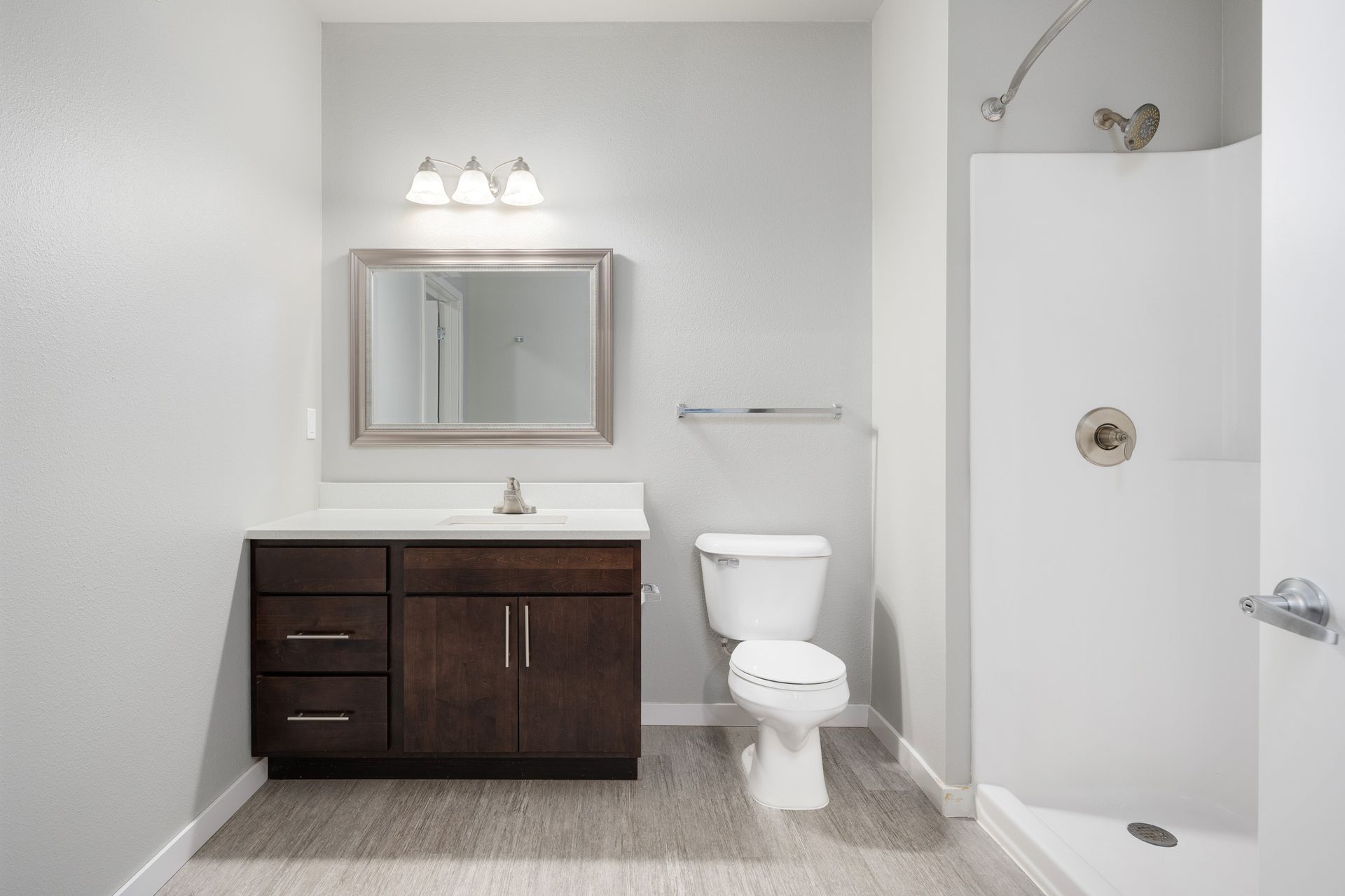 Bathroom with a white shower, toilet, dark brown vanity, and a gray floor.