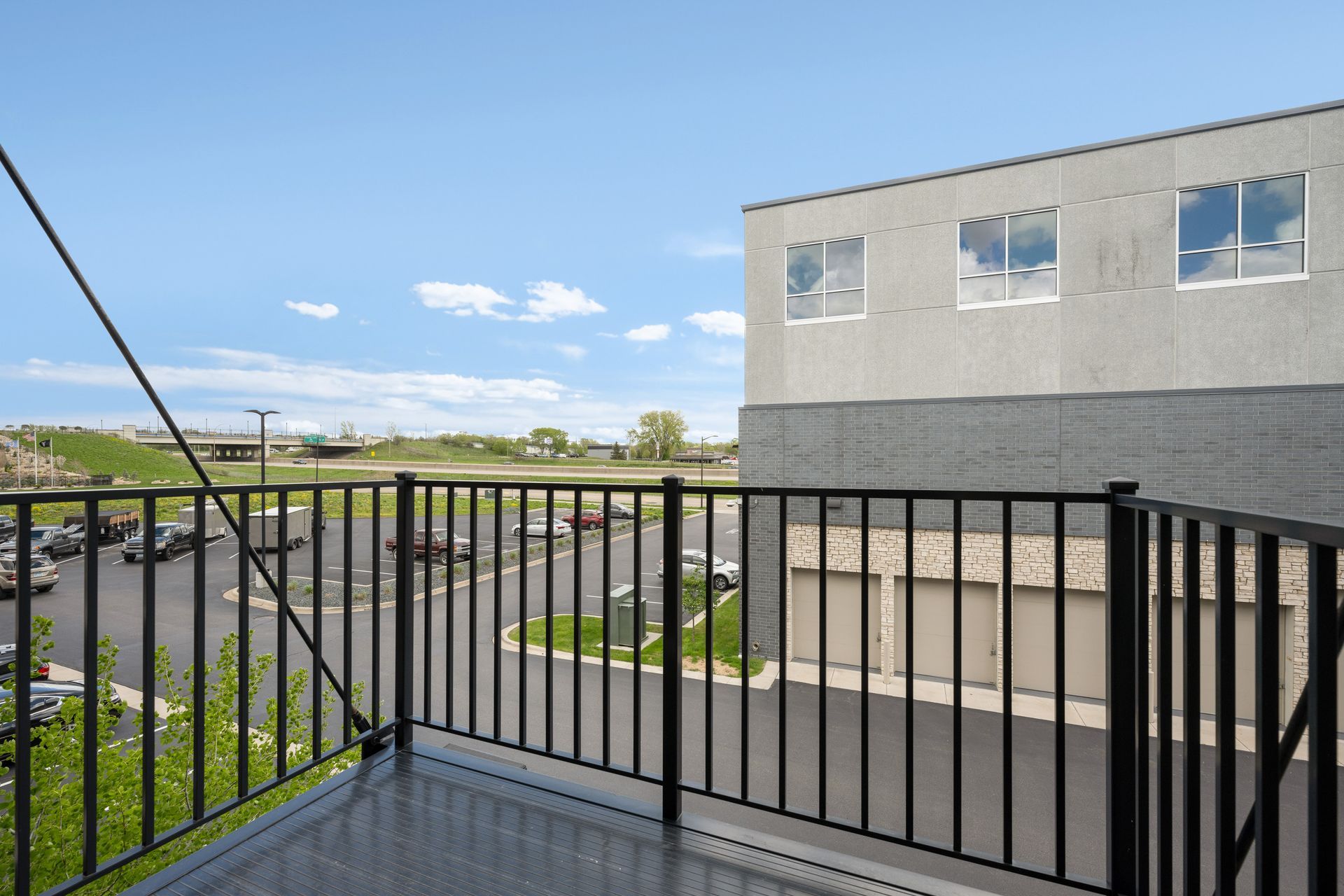 Balcony overlooking parking lot and building with windows, under blue sky.