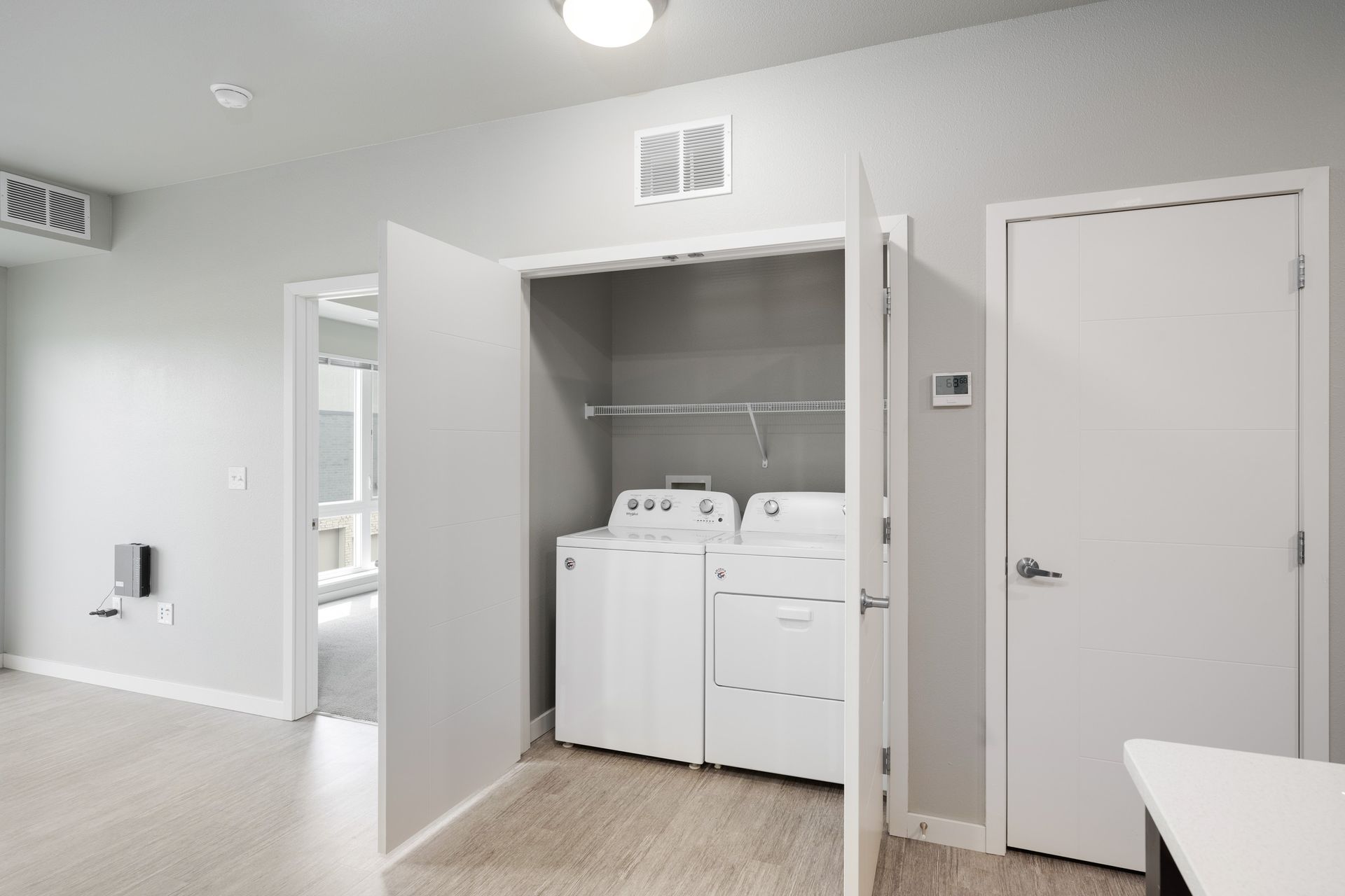 Laundry closet with washer and dryer, open doors, and hallway visible. White appliances and walls.