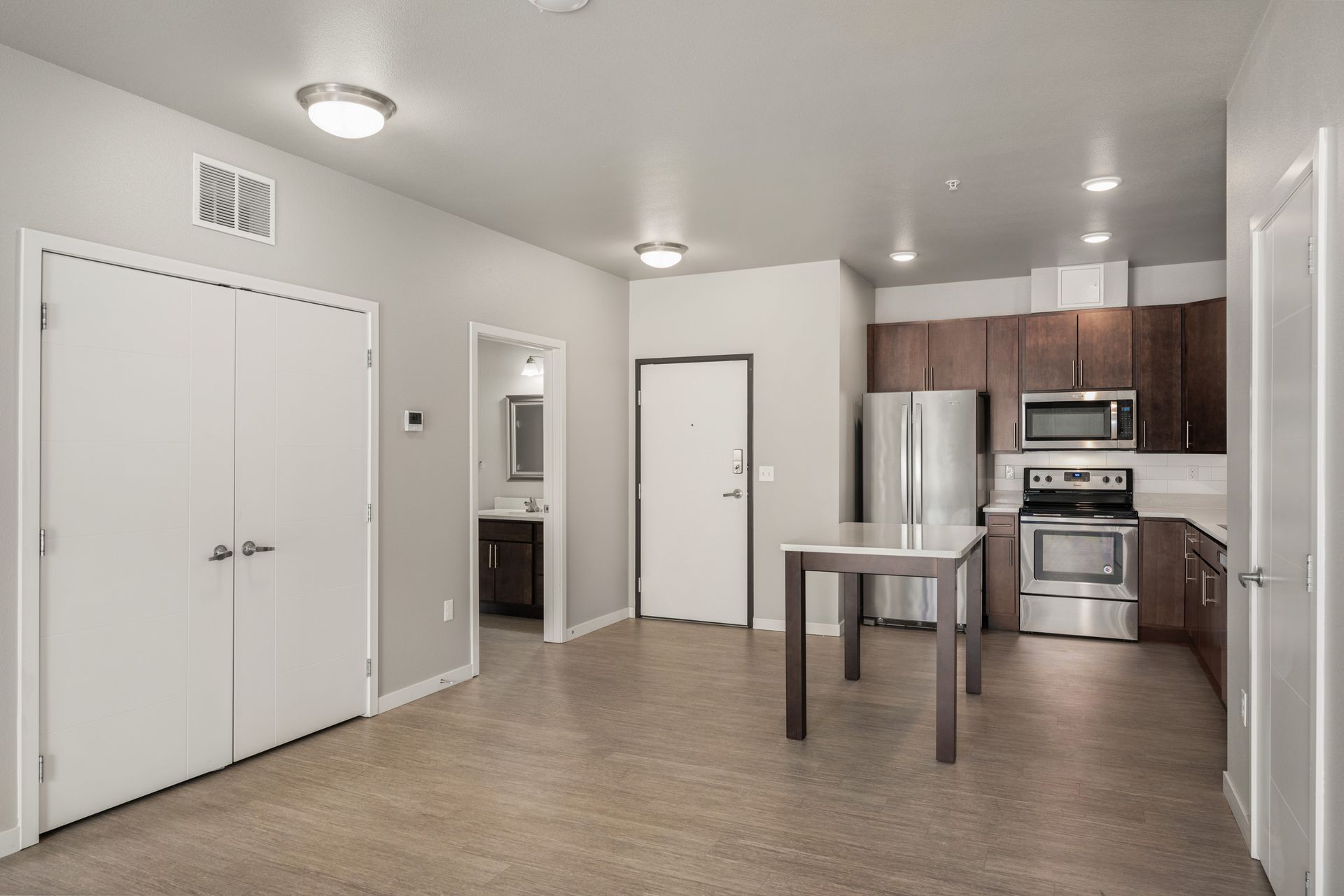 Interior view of a modern apartment with kitchen, dining area, and closet. Brown cabinets and stainless steel appliances.