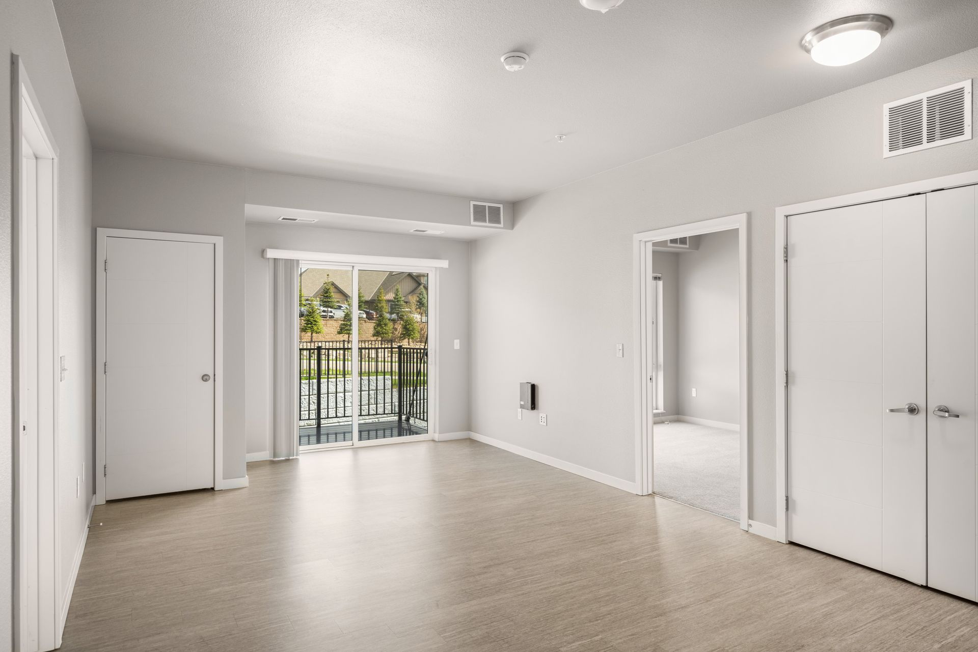 Empty, bright room with doors, a balcony, and neutral-colored flooring and walls.