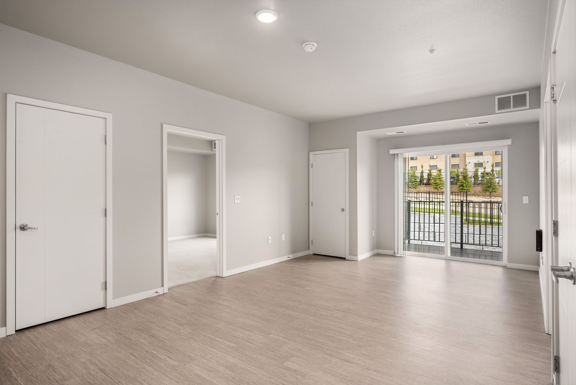 Empty room with light gray walls, wood-look floor, and a balcony with a black railing.