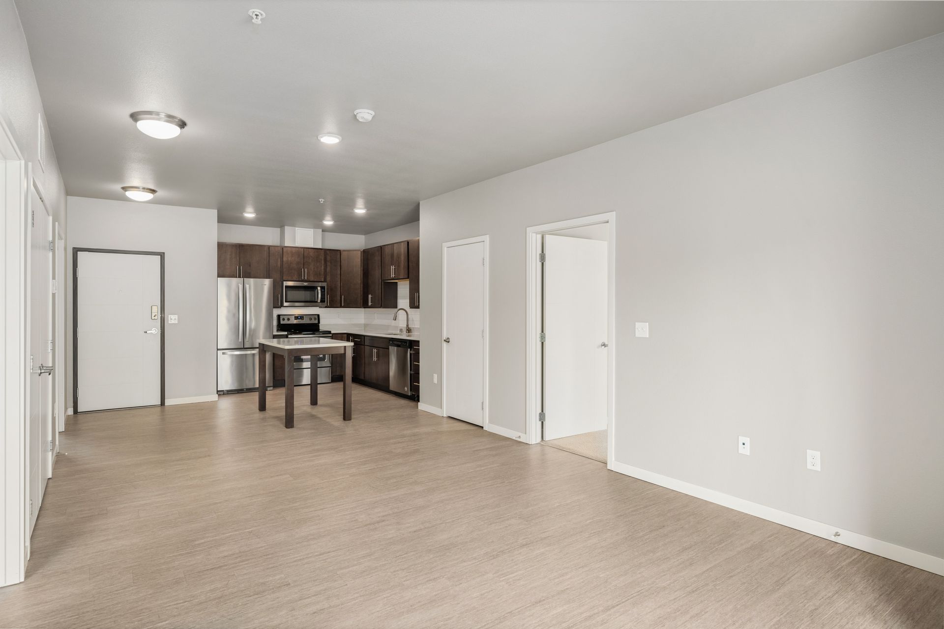 Open-plan apartment interior with a kitchen, dining area, and living room. Neutral colors and natural light are present.
