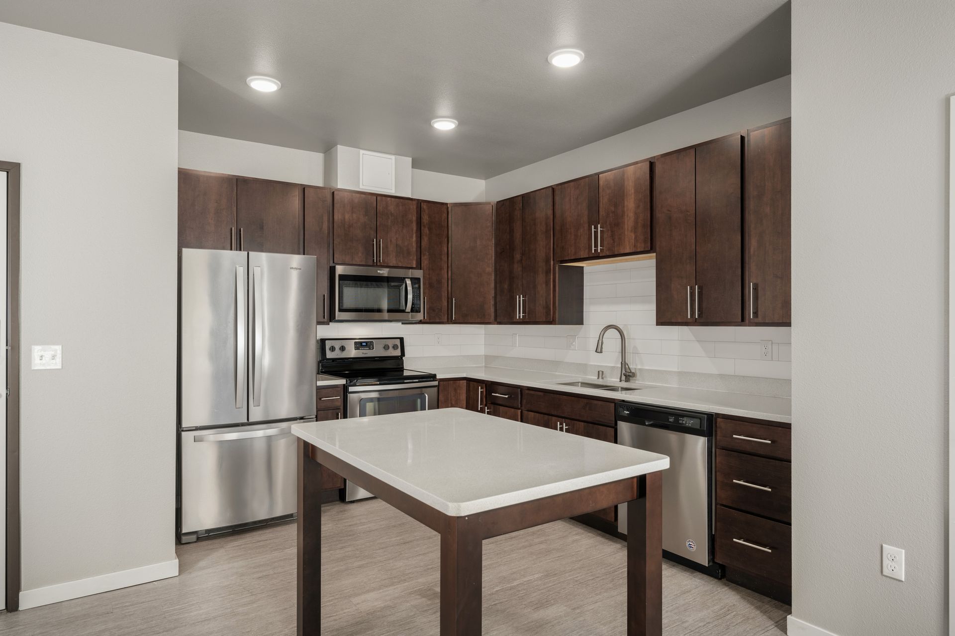 Modern kitchen with dark wood cabinets, stainless steel appliances, and white countertop island.