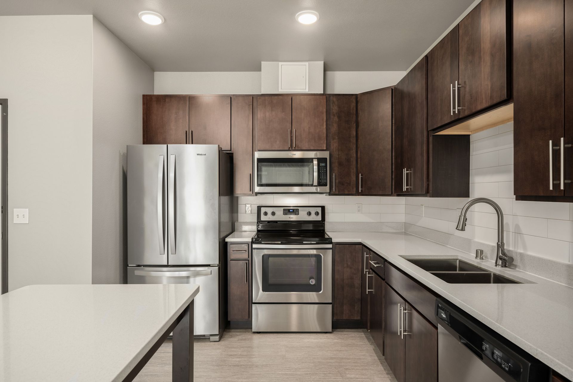 Modern kitchen with dark brown cabinets, stainless steel appliances, and a white countertop.
