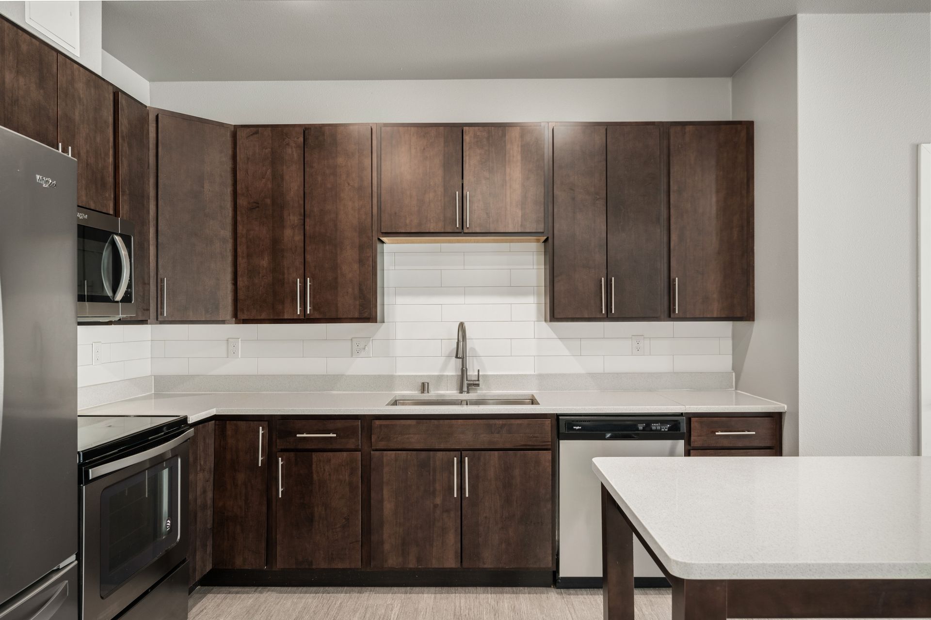 Kitchen with dark wood cabinets, stainless steel appliances, white countertops and backsplash.