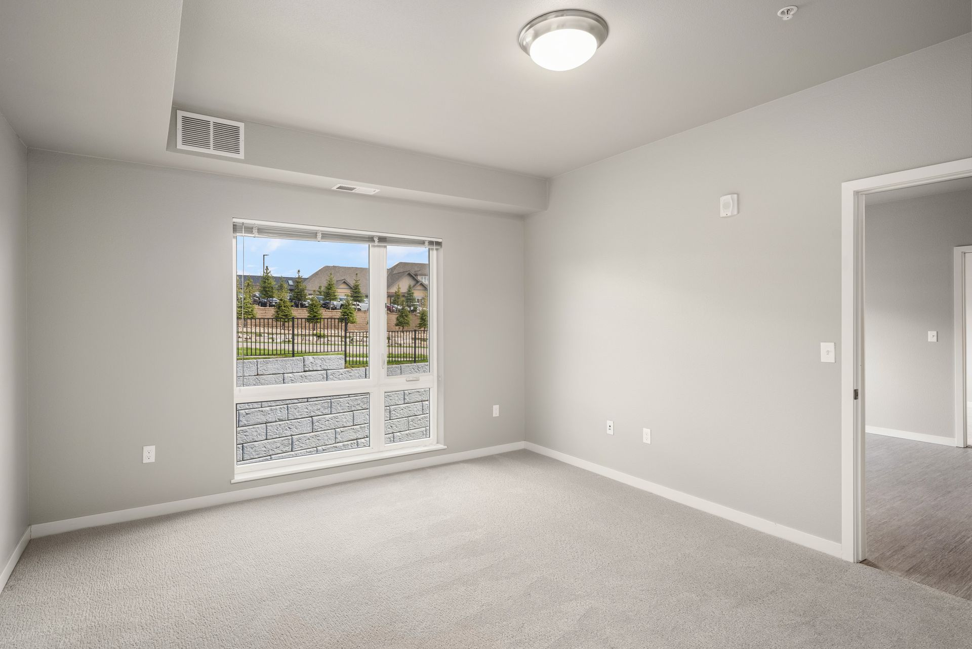 Empty room with a window and door, light gray walls and carpet.