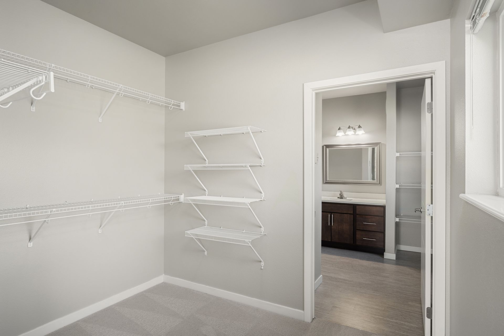 Walk-in closet with wire shelving and an open doorway to a bathroom with a vanity and mirror.