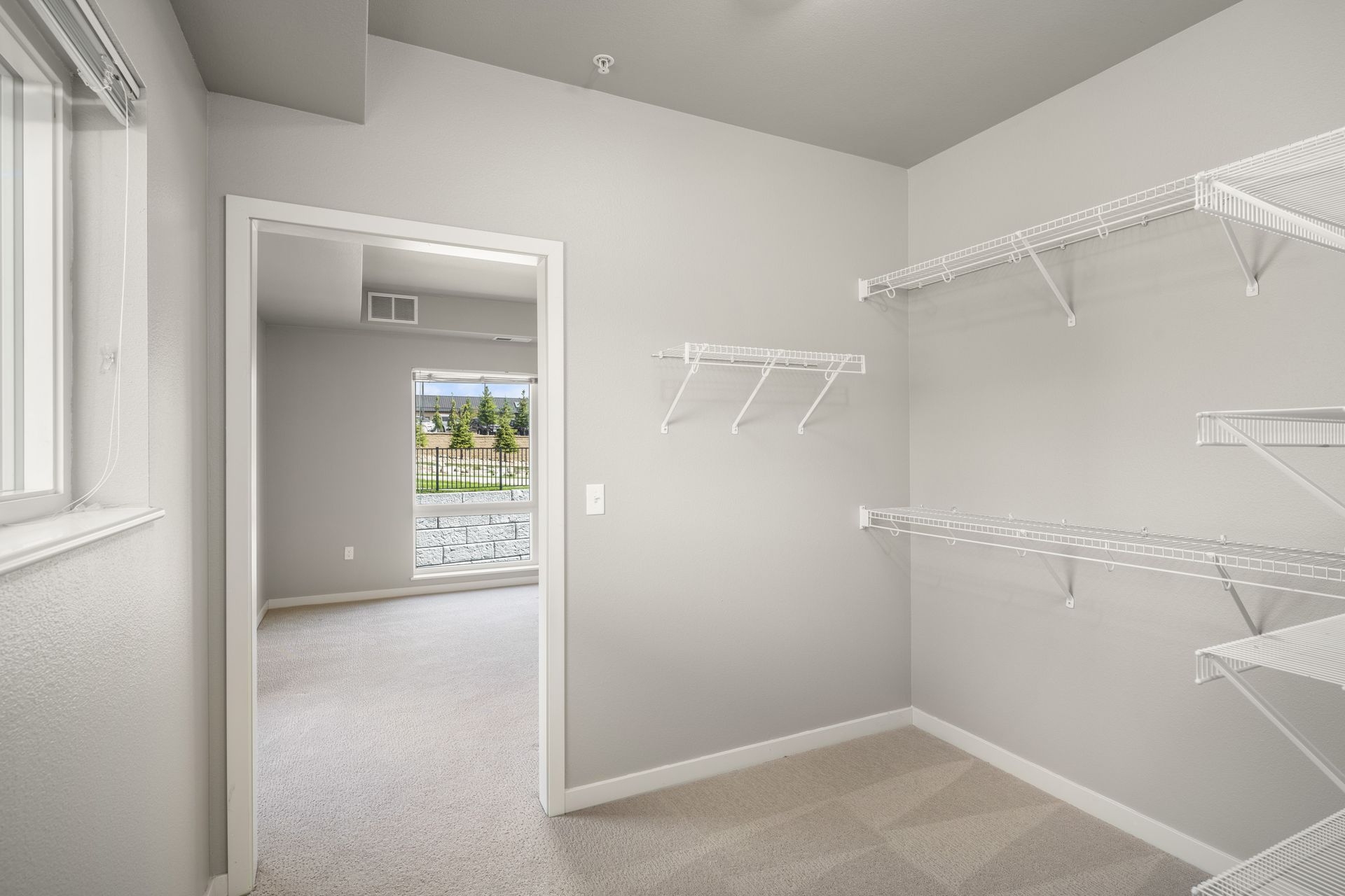 Walk-in closet with wire shelving and an open doorway to a bedroom with a window. Gray walls and carpet.