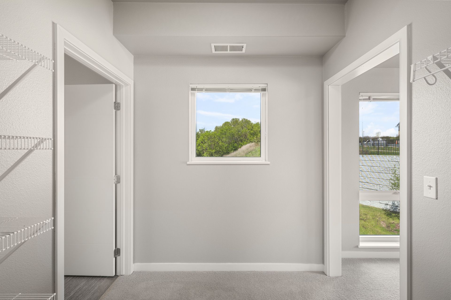 Hallway with doors, a window with a view, and wire shelving. Gray walls and carpet.