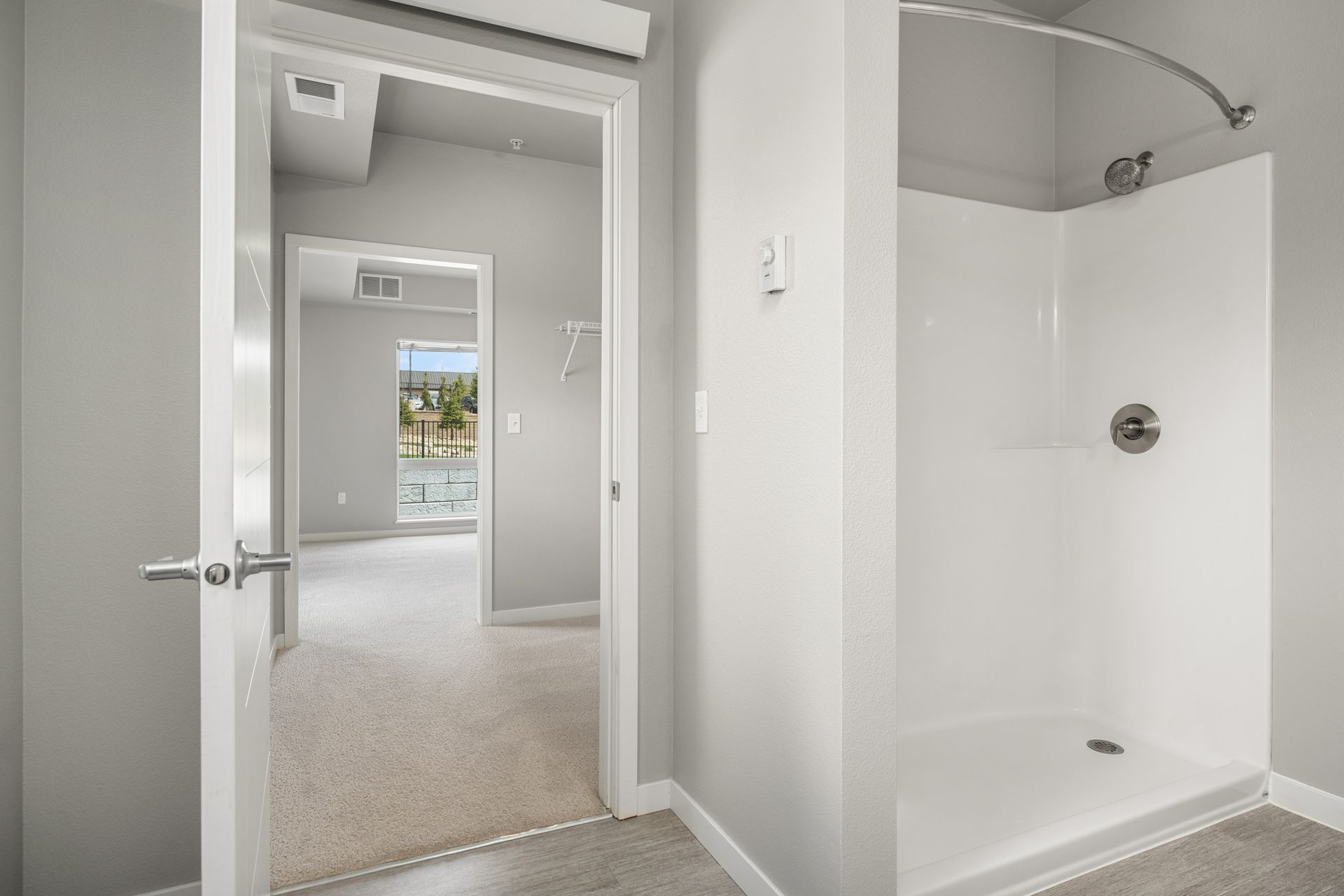 Bathroom with white shower stall and open doorway to bedroom with carpet.