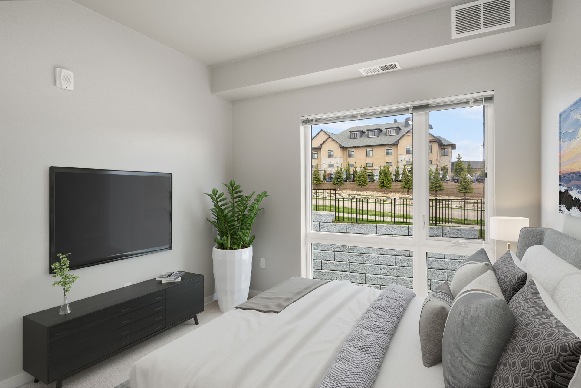 Bedroom interior with a bed, TV, and large window overlooking a neighborhood.
