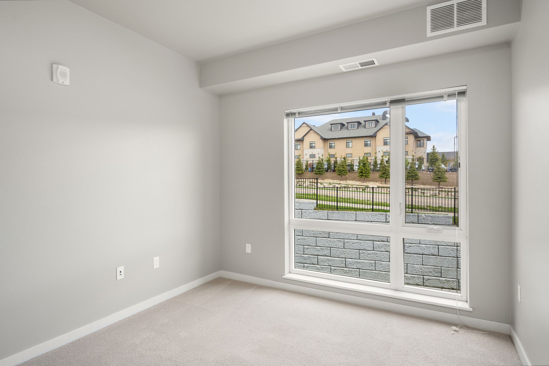 Empty room with a large window. Neutral-colored walls, carpet. View through the window shows other buildings.