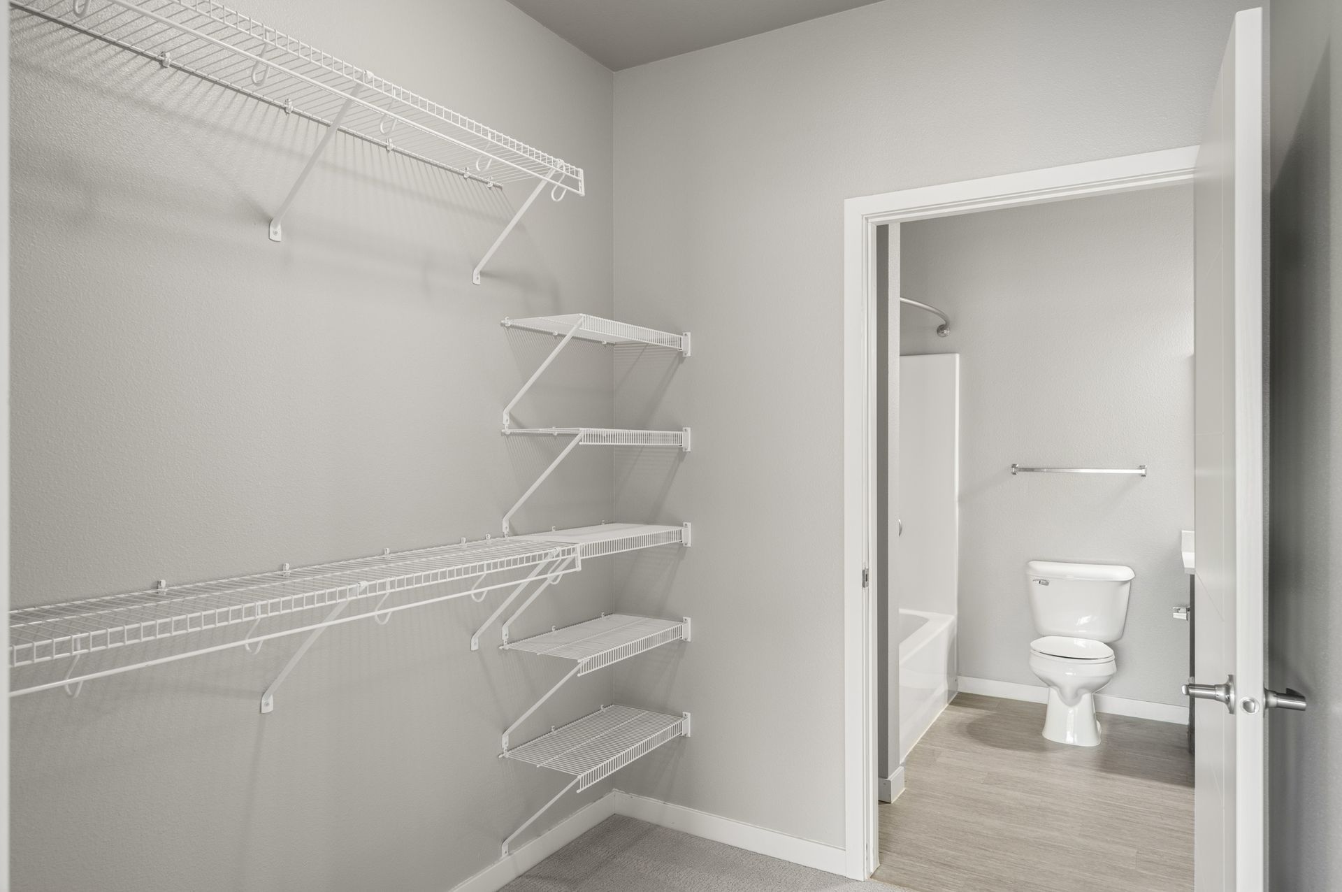 Empty walk-in closet with wire shelving, door open to a bathroom with a toilet and shower.