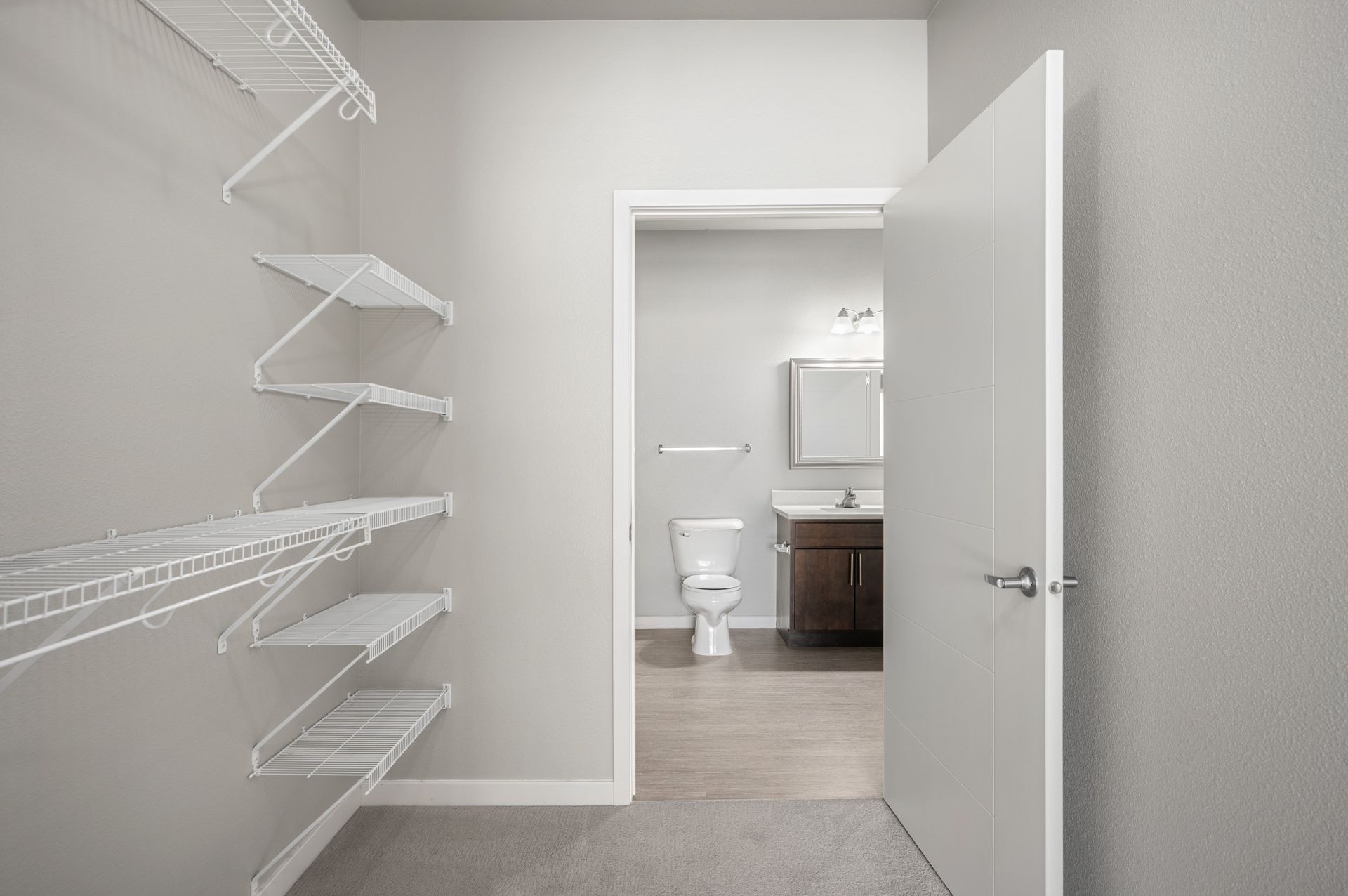Walk-in closet with wire shelves and doorway to a bathroom with a toilet and vanity.