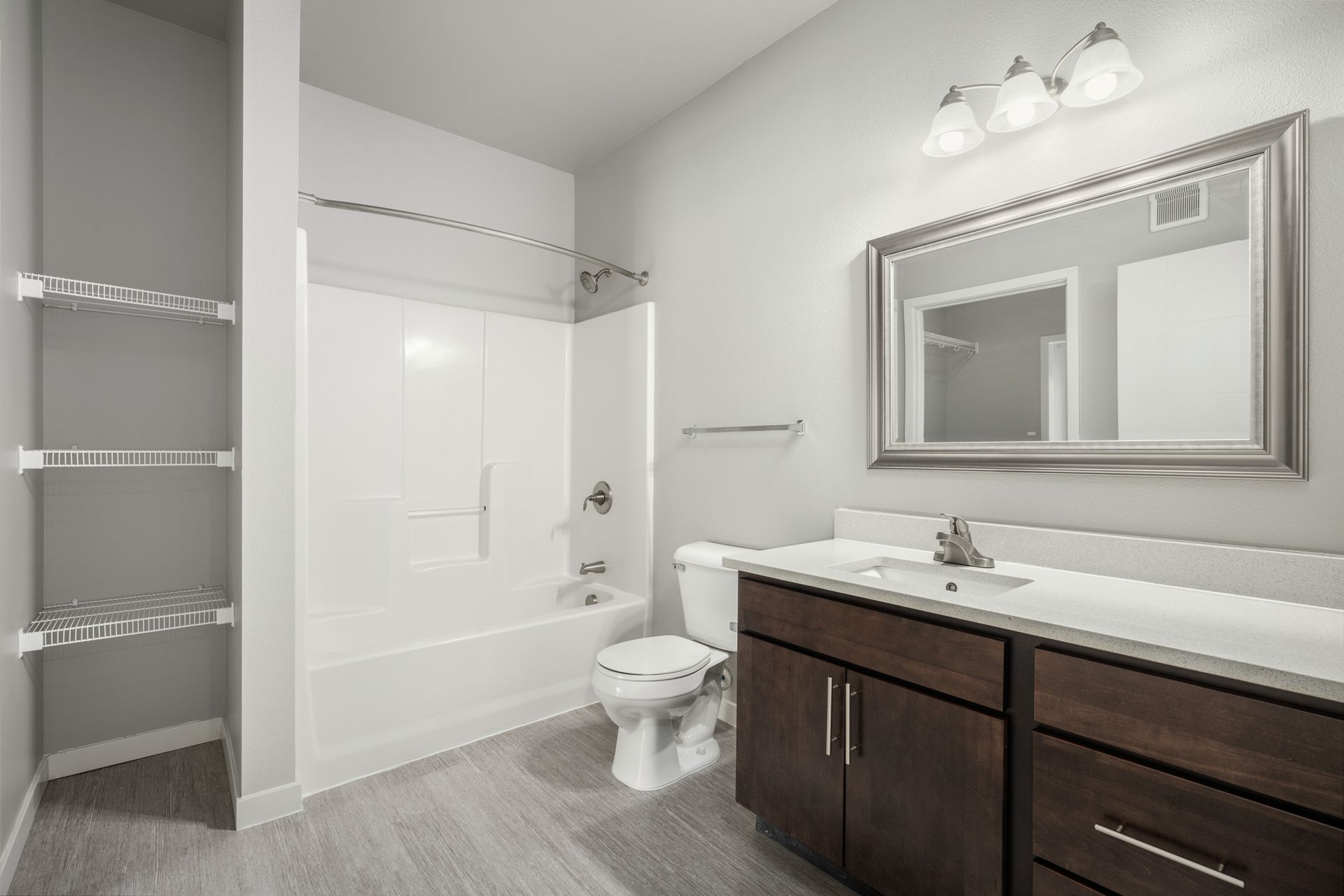 Bathroom with a white tub and shower, toilet, dark wood vanity, and a large mirror.