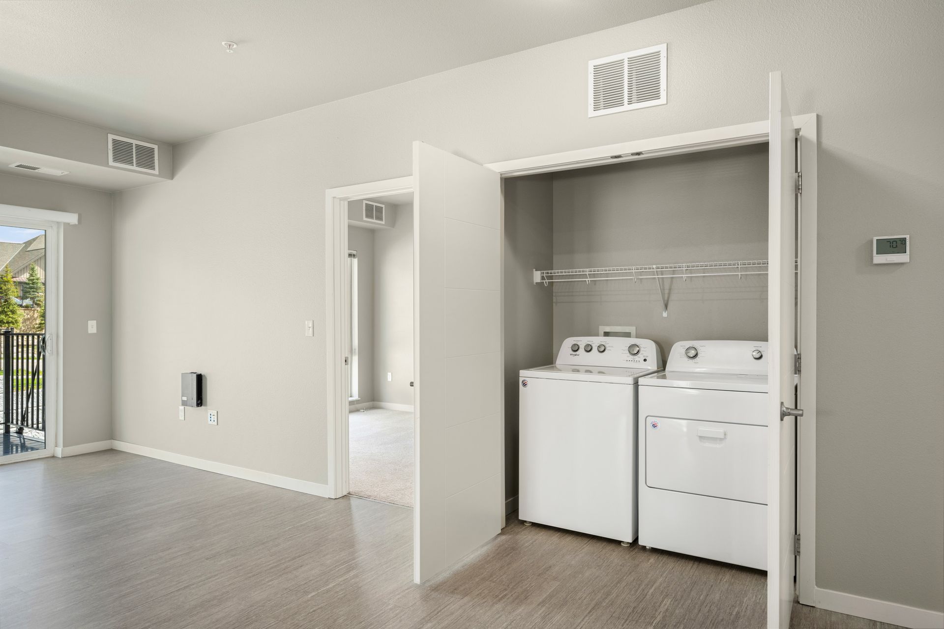 Laundry closet with white washer and dryer, open white door, light grey walls, and hardwood floors.