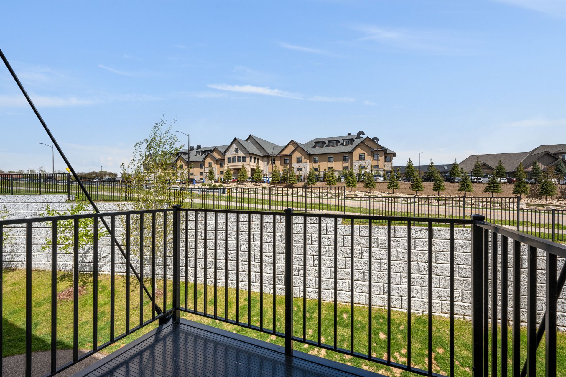 View of homes across a lake from a patio with a black railing on a sunny day.