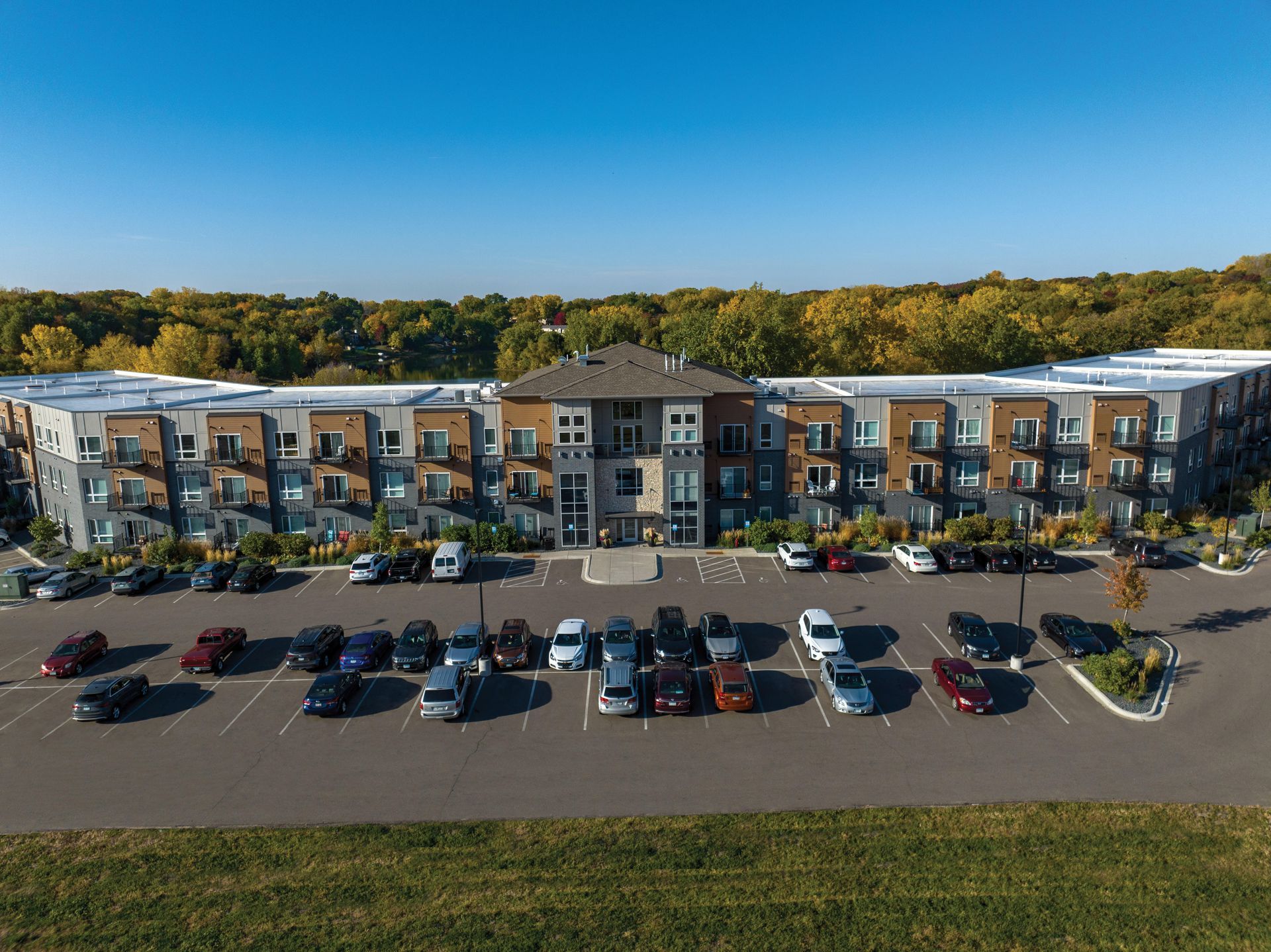 Apartment building with cars parked in front, clear blue sky and trees in the background.