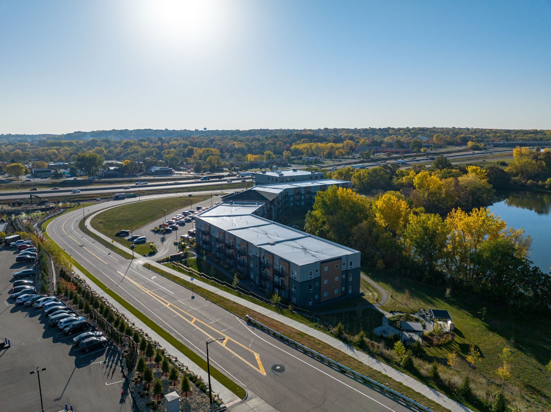 Aerial view of modern apartment building near a curved road and river on a sunny day.