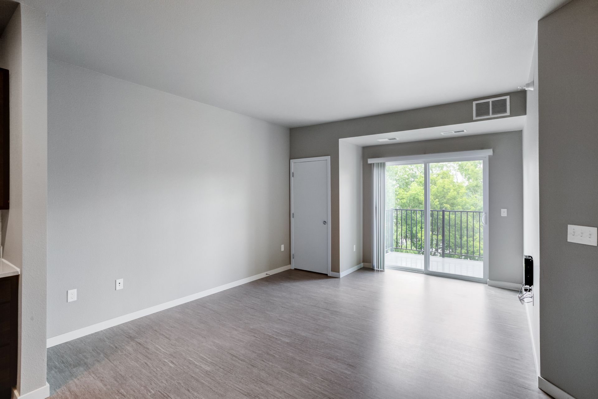 Empty living room with gray walls, wood-look floor, and a sliding glass door to a balcony.