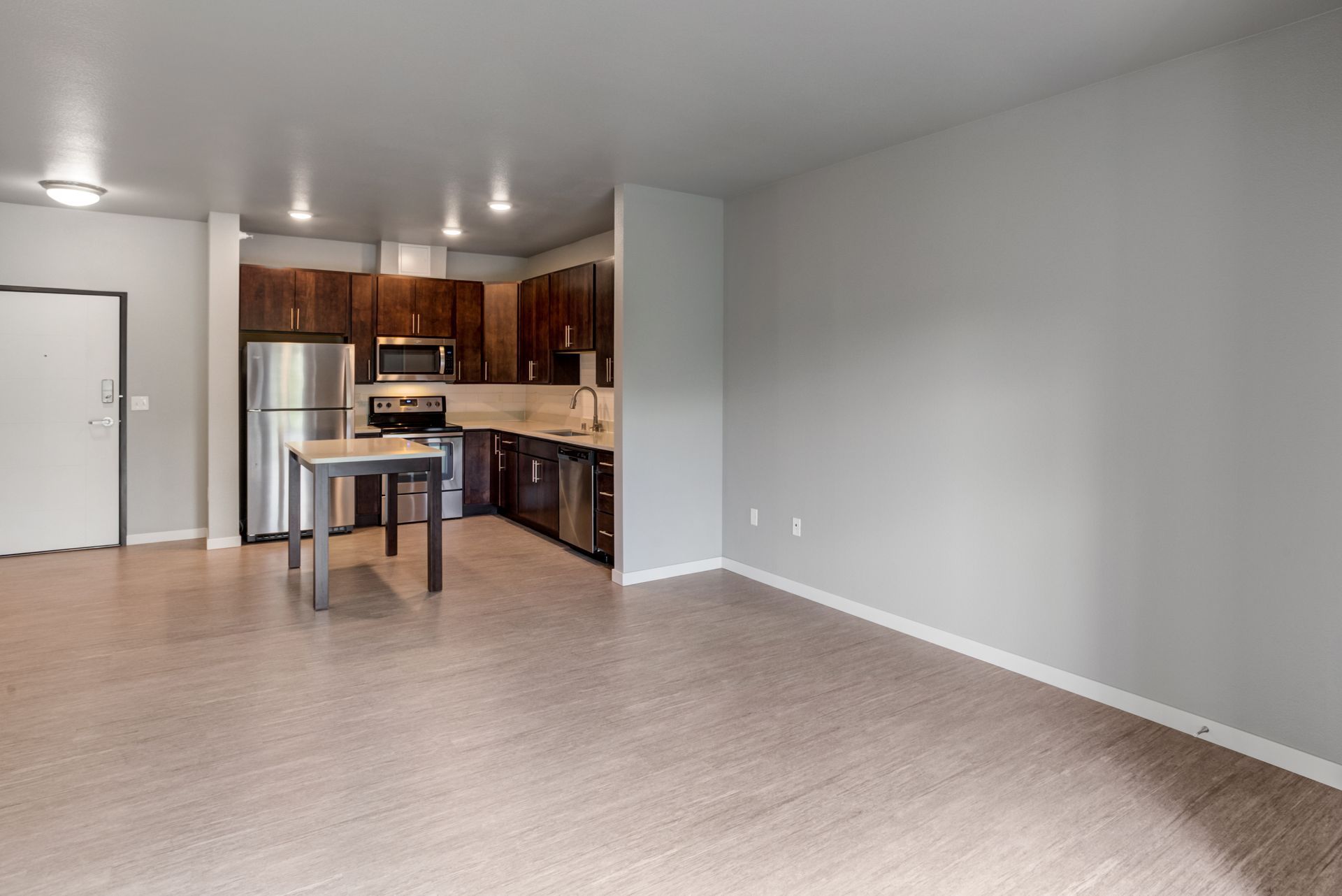 Empty apartment interior with kitchen, stainless steel appliances, and gray walls.
