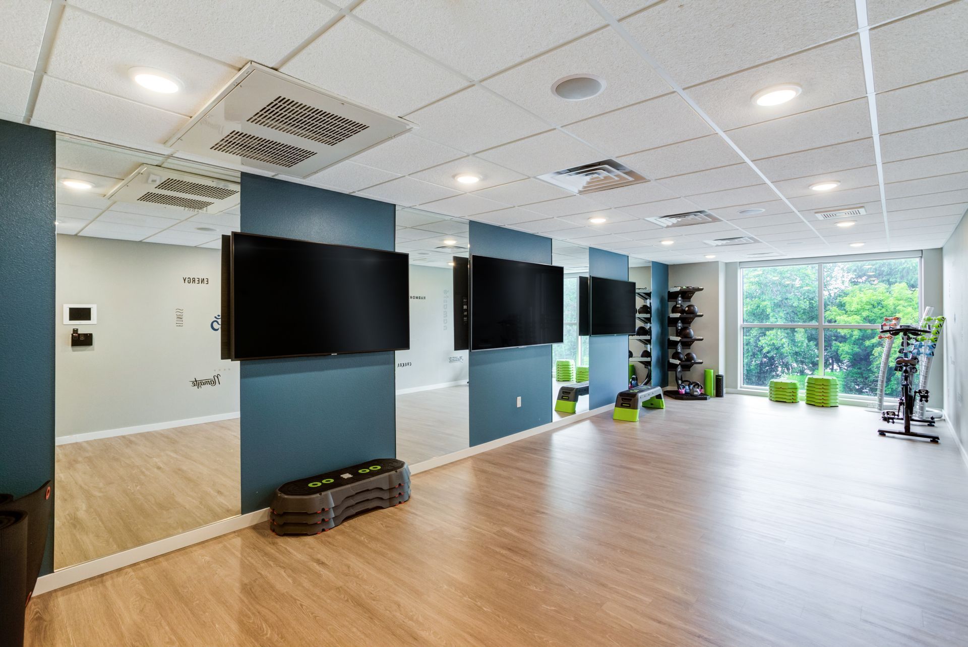 Gym interior with mirrors, TVs, exercise equipment, and wood-look flooring.