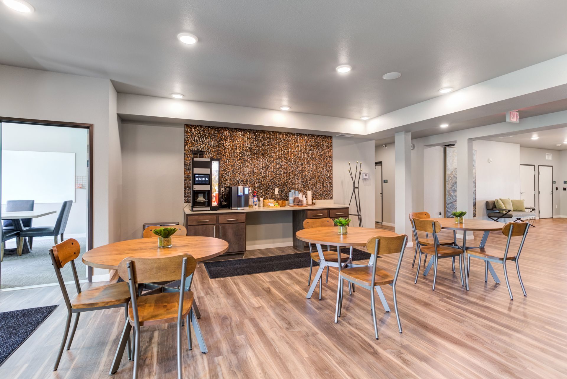 Coffee bar with round tables, wooden chairs, and a coffee machine in a neutral-toned room.