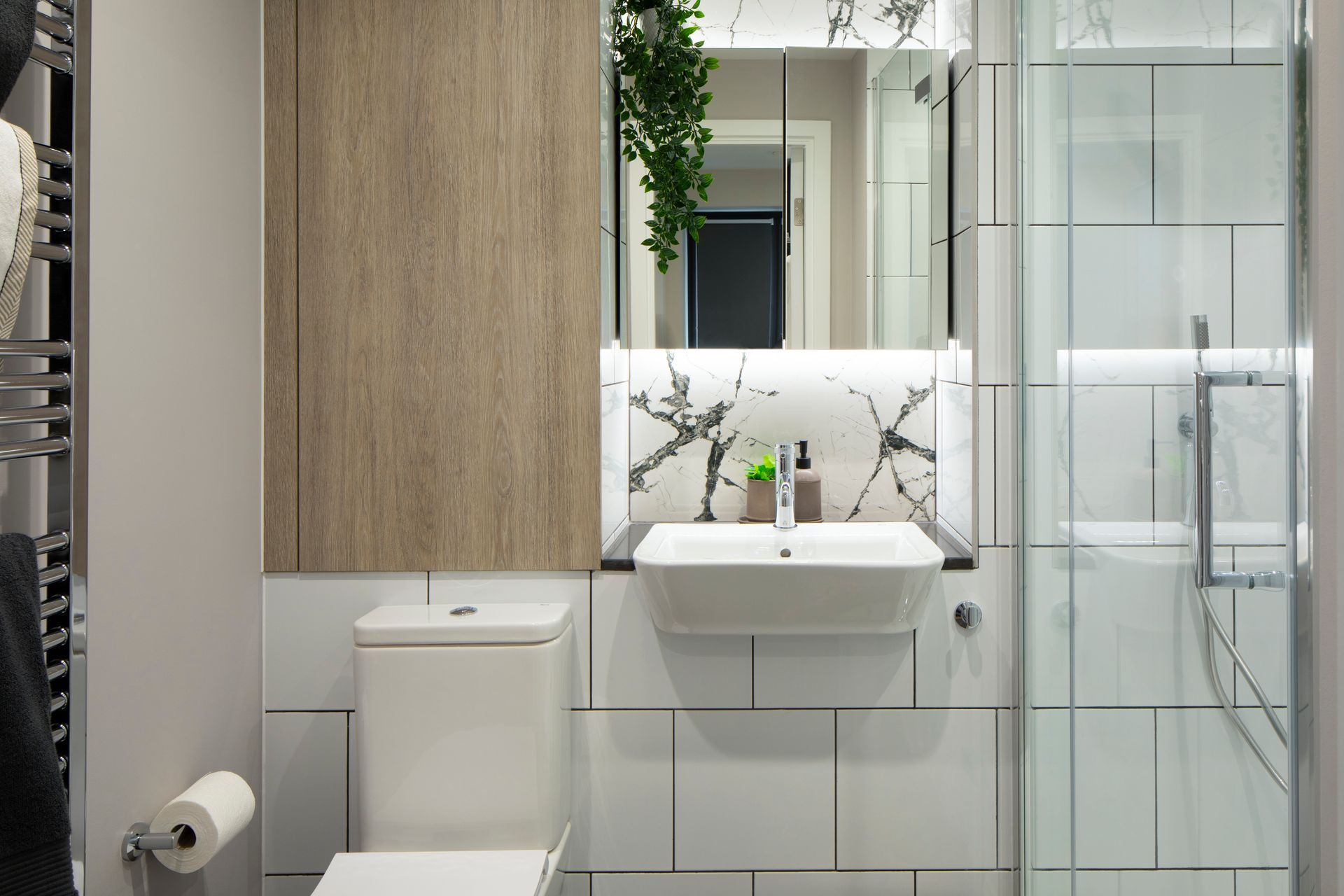 A modern bathroom with a white sink, toilet, glass-enclosed shower, wood paneling, and marble backsplash.