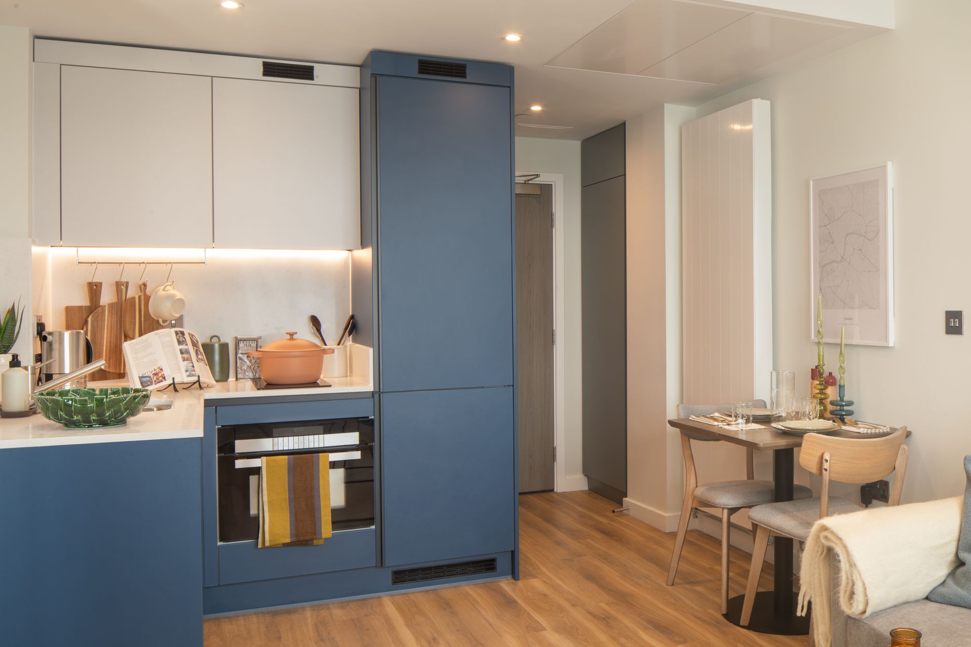 Modern kitchen featuring blue cabinetry, a built-in oven, white upper cabinets, and a small dining table in the corner.