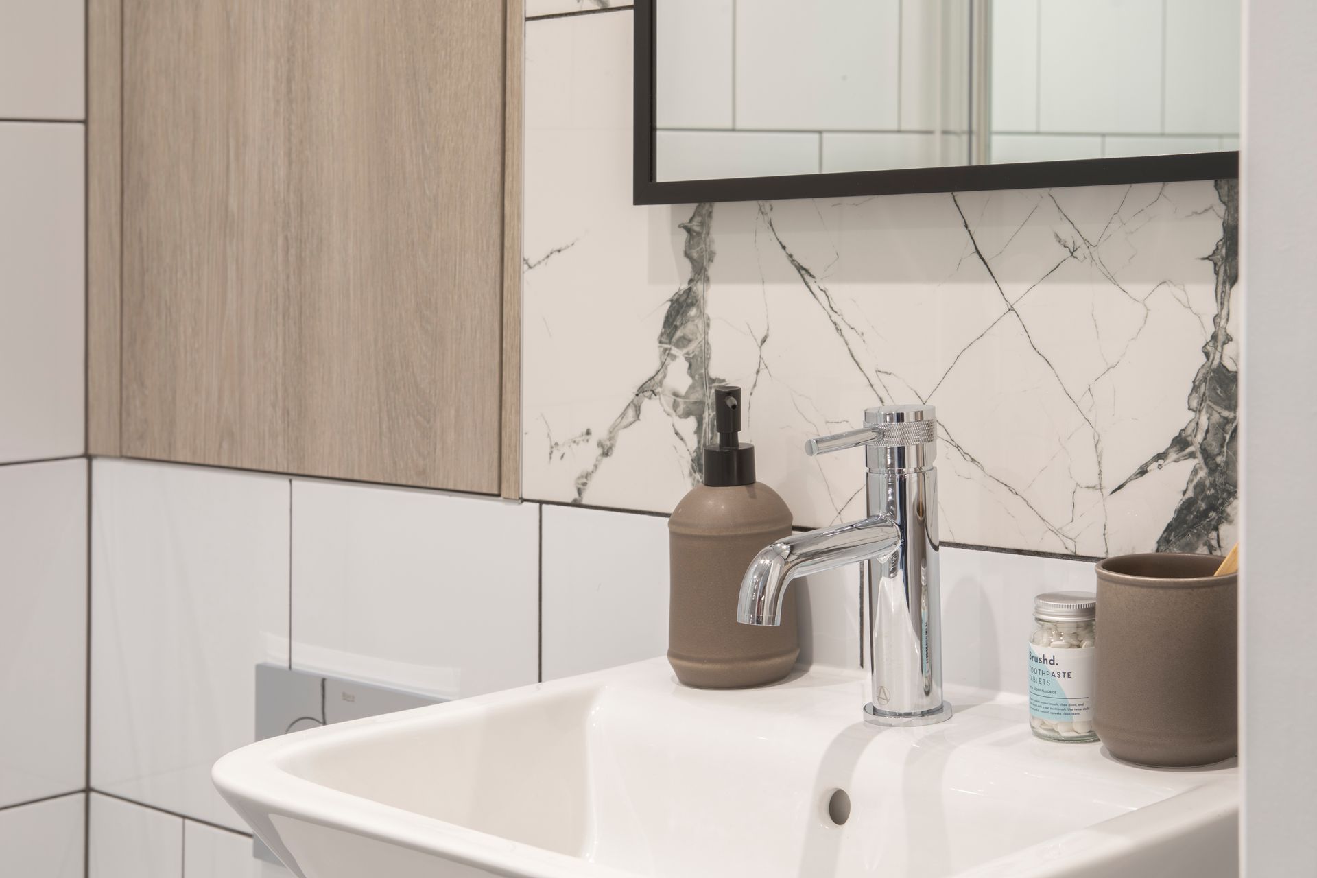 A bathroom sink area with a chrome faucet, a brown soap dispenser, a toothbrush holder, and marble-style wall tiles.