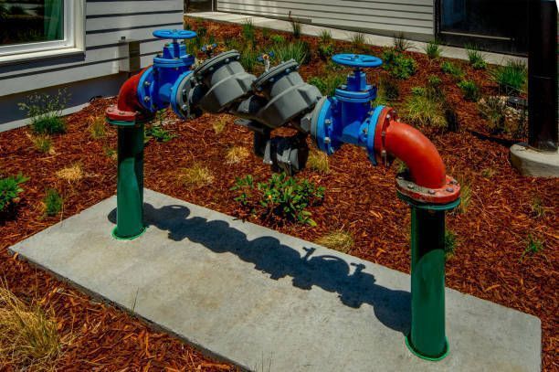 Water pipes with blue valves, connected with gray components, and red bends on green posts over concrete pad.