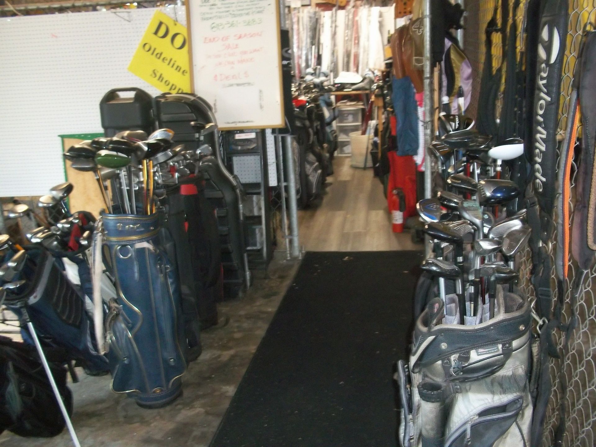 A narrow storage space lined with several golf bags filled with clubs on both sides of a central mat.