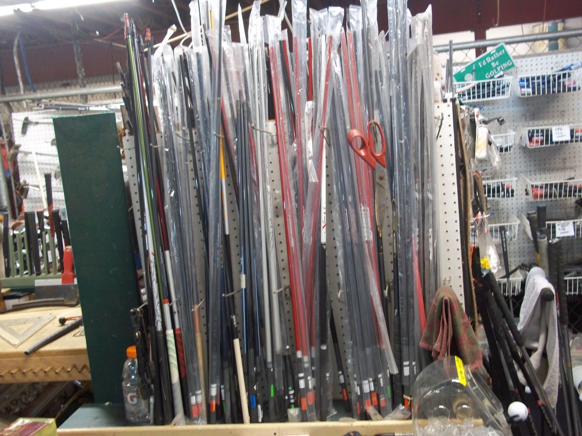 A collection of various fishing rods stored upright in plastic sleeves on a pegboard rack in a store.